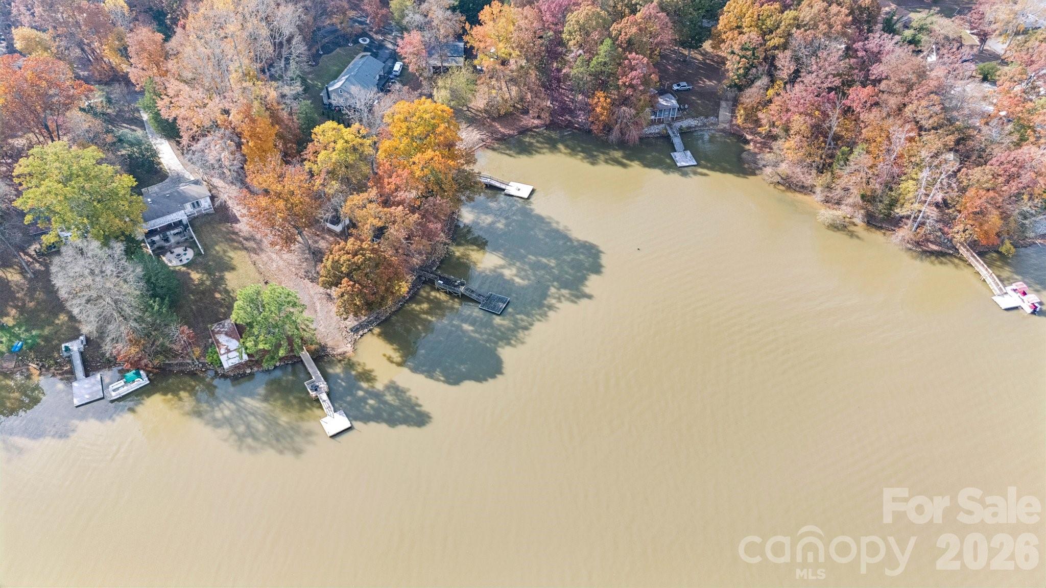 Aerial view of lakefront homes and docks along a wooded shoreline in autumn.