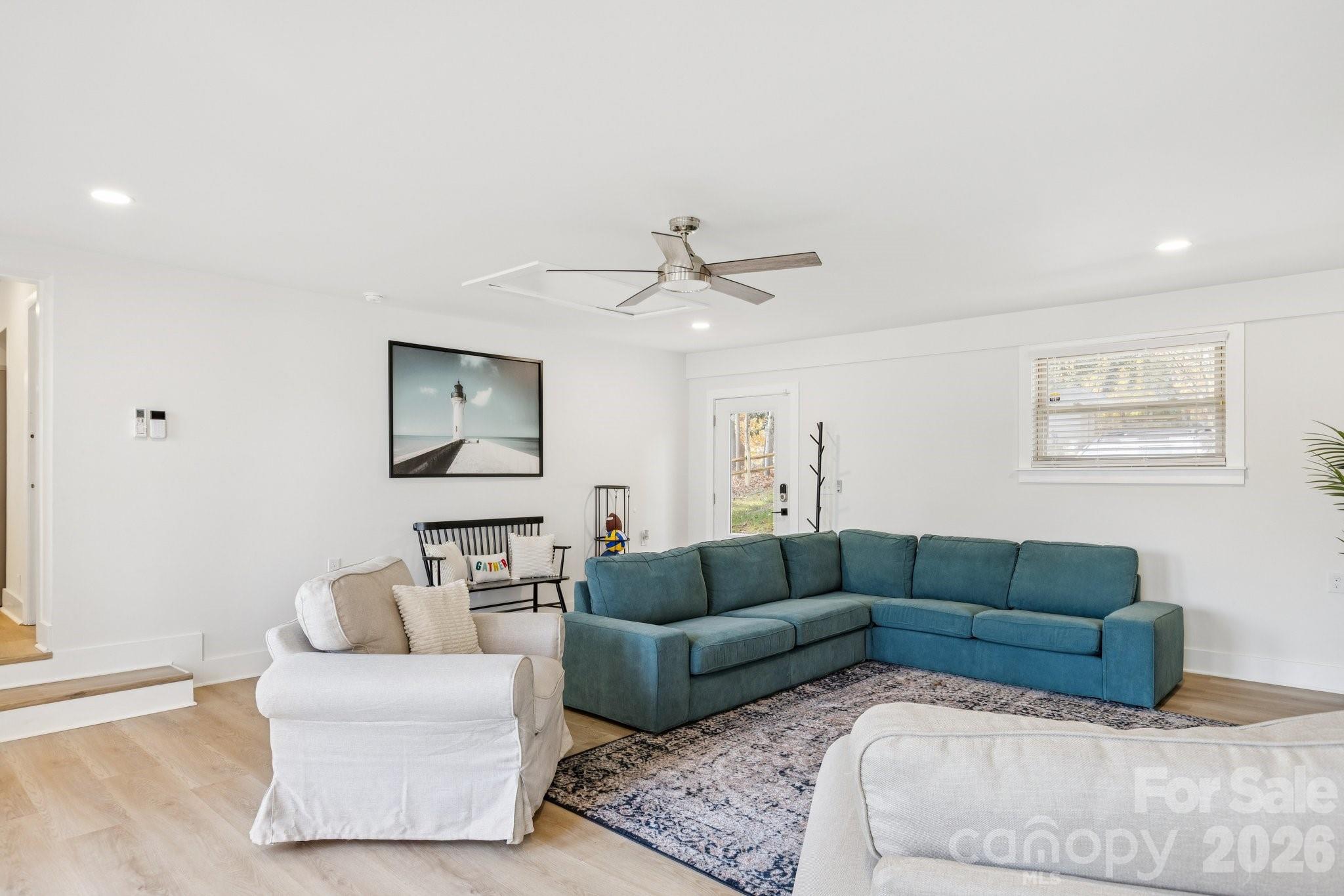 Living room with a teal sectional, white armchairs, patterned rug, and light wood floors.