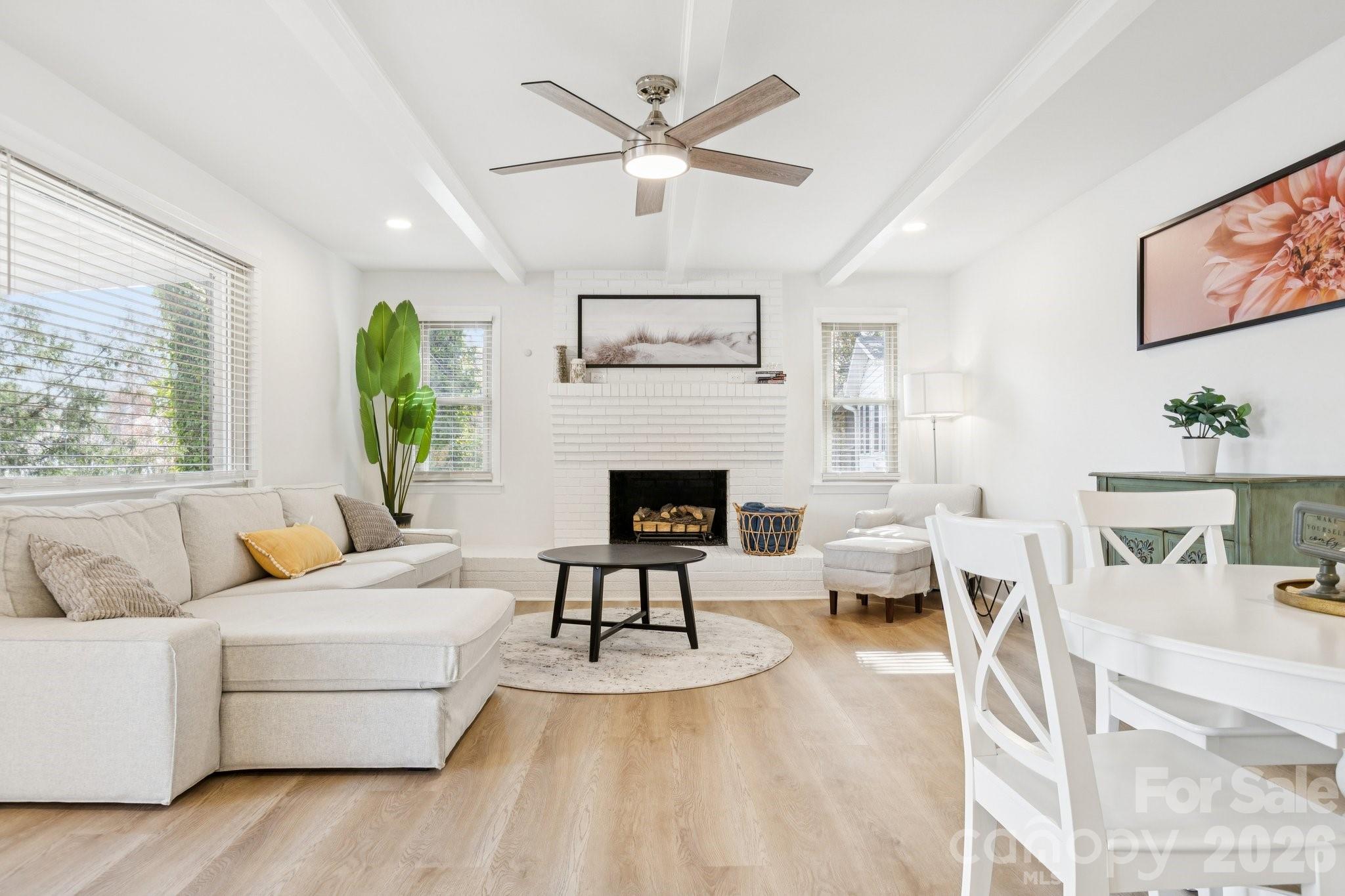 Staged living room with a white sectional, brick fireplace, and dining area in the foreground.