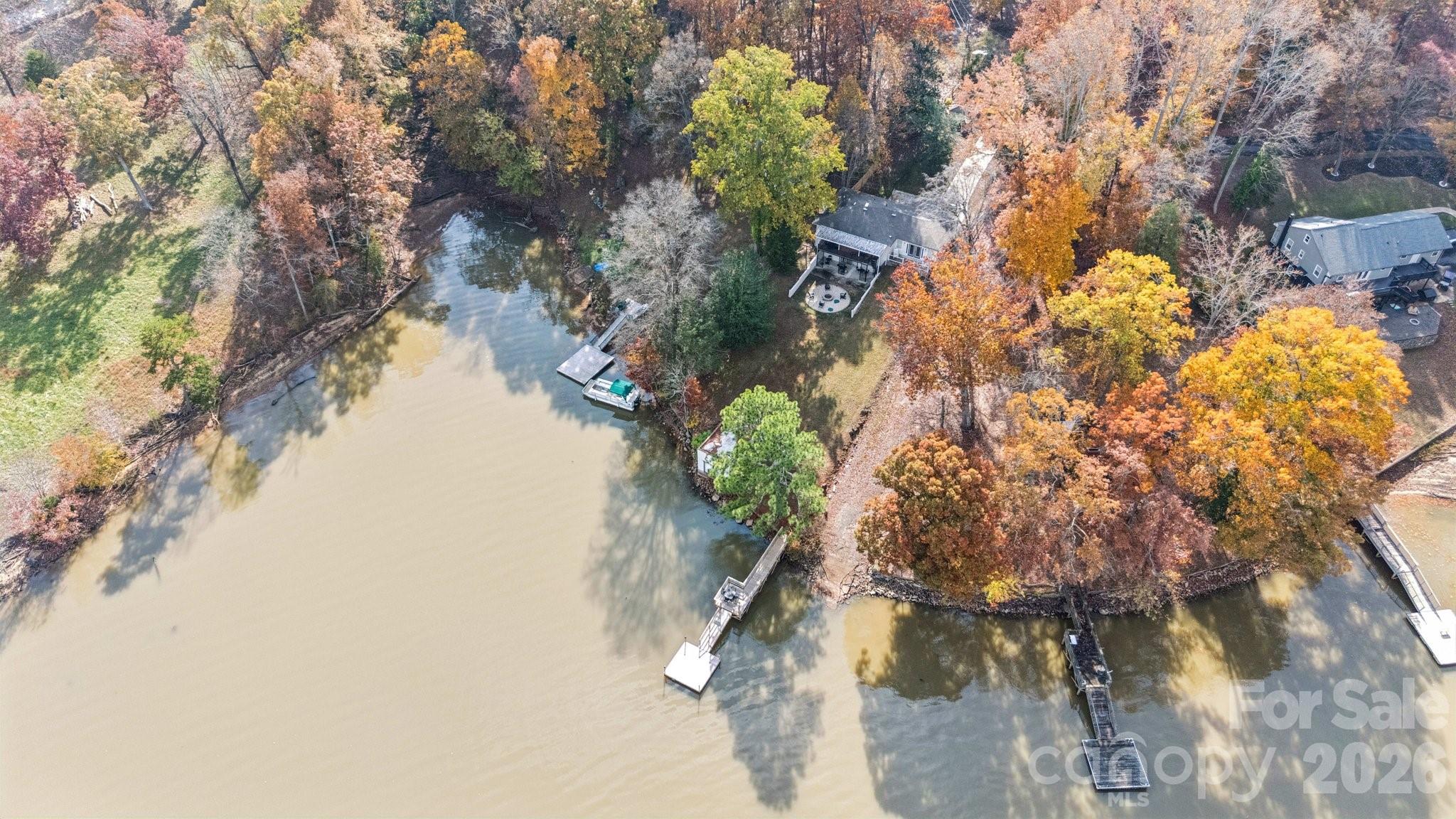 Aerial view of a waterfront house with a private dock and colorful autumn trees.