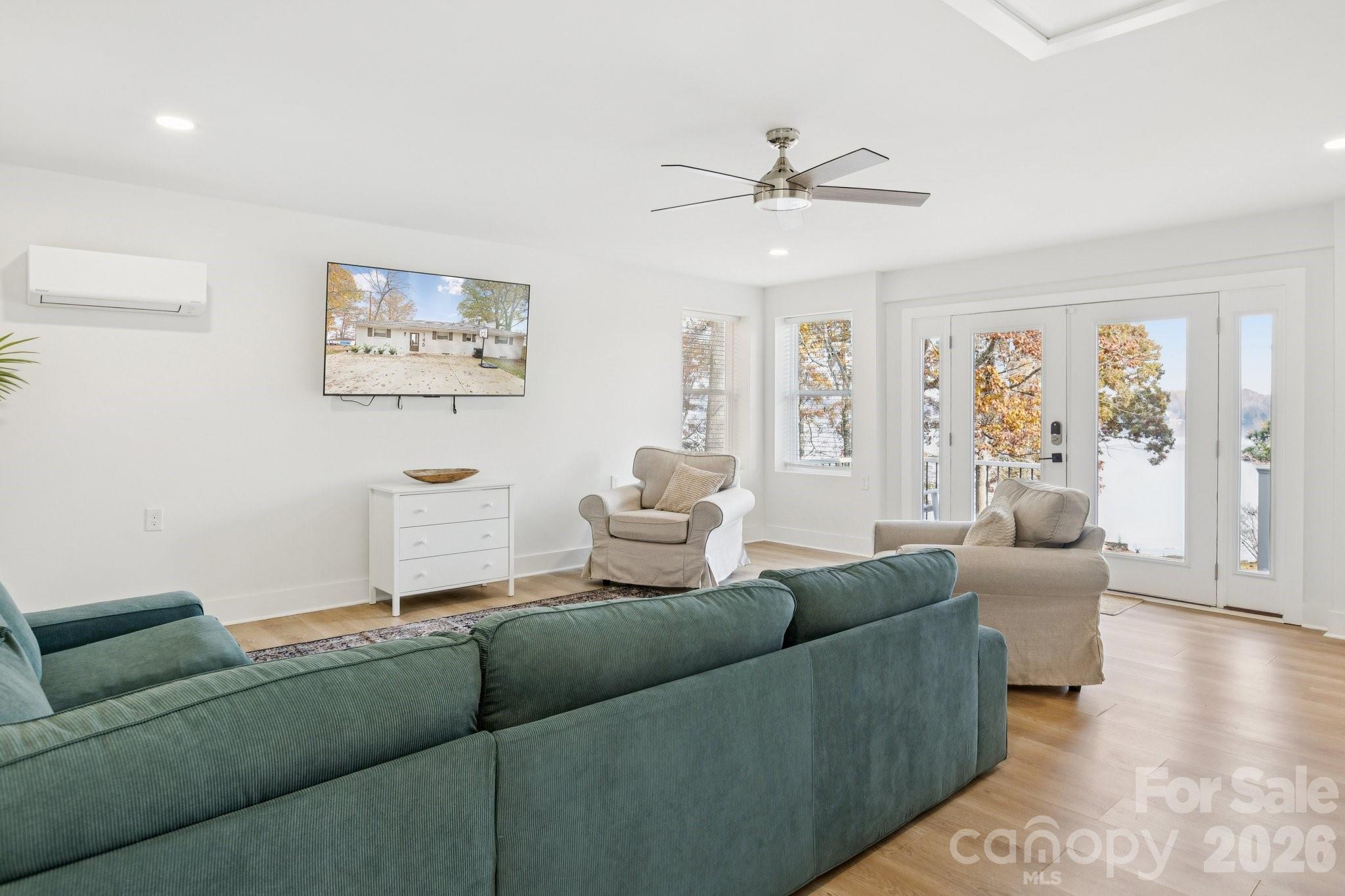 Furnished living room with a teal sectional, beige armchairs, and French doors overlooking autumn trees.
