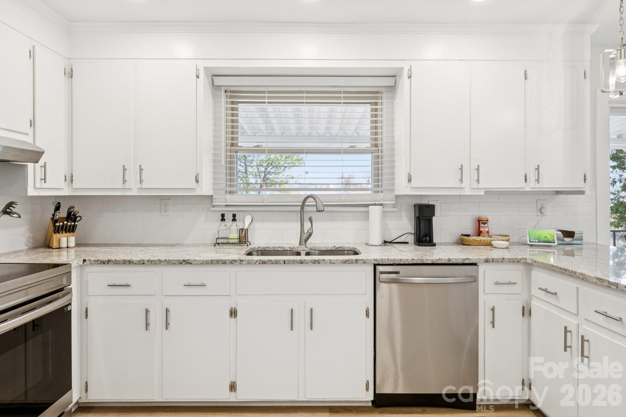 White kitchen with stone counters, stainless appliances, and a sink beneath a window.