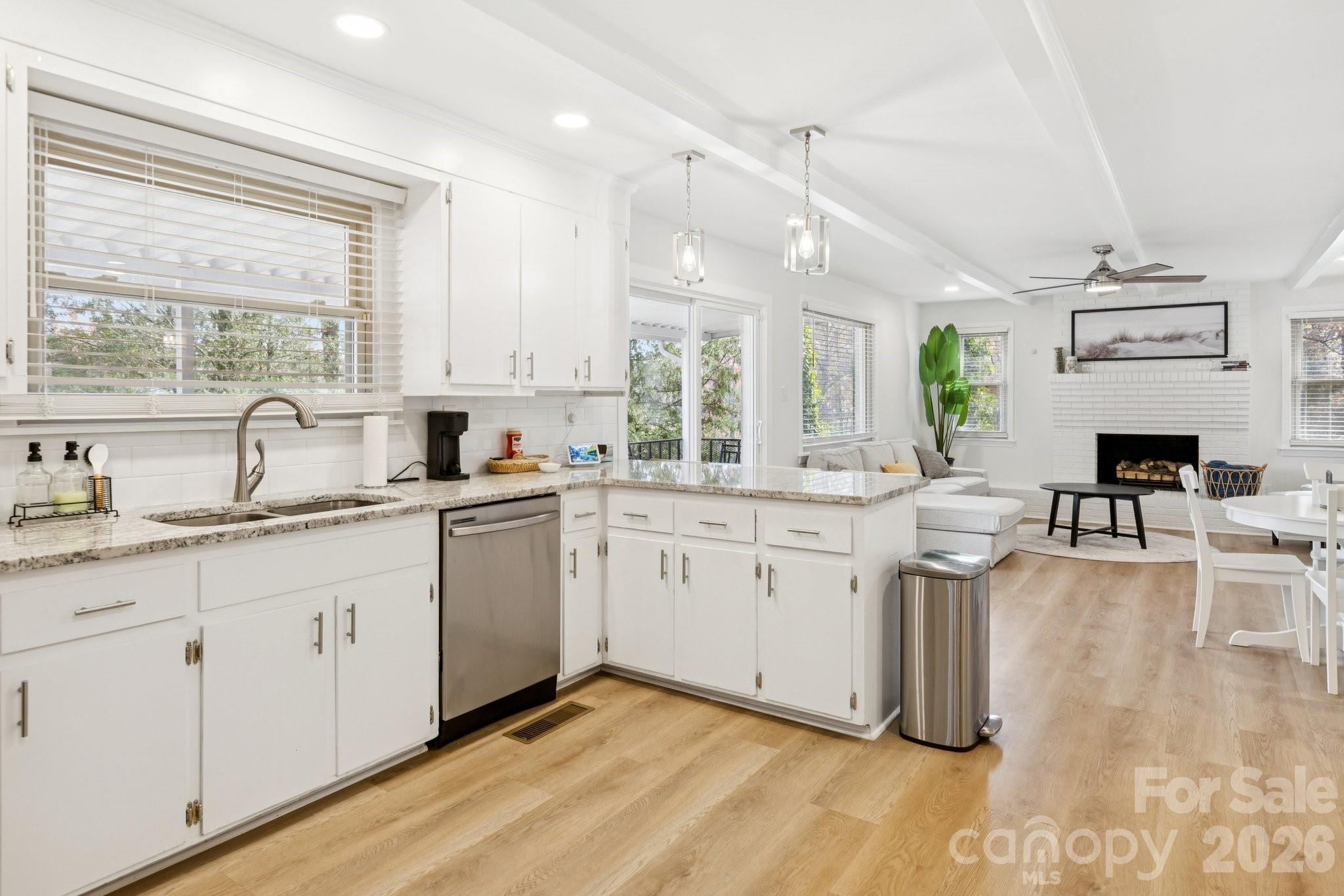 Bright white kitchen with granite island opening onto a living room with a white brick fireplace.