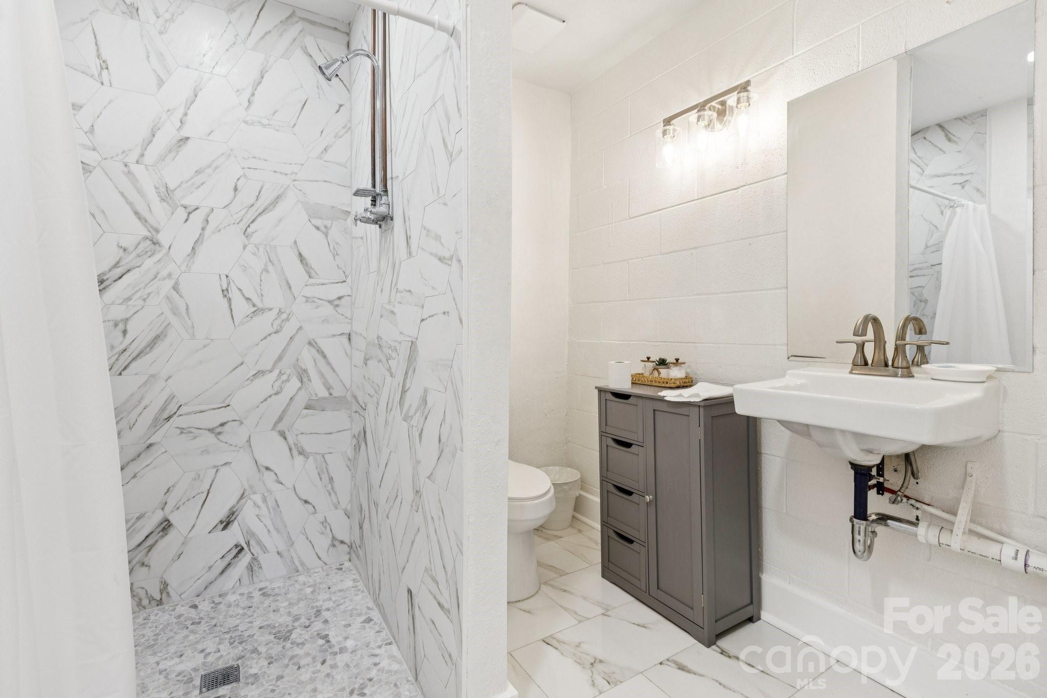Bathroom with a marble-look hex-tile shower, gray cabinet, and wall-mounted sink.