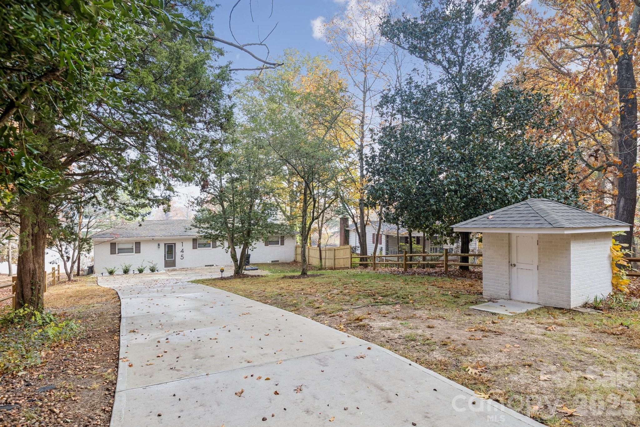 Single-story white brick home with a curved driveway, mature trees, and a detached outbuilding.