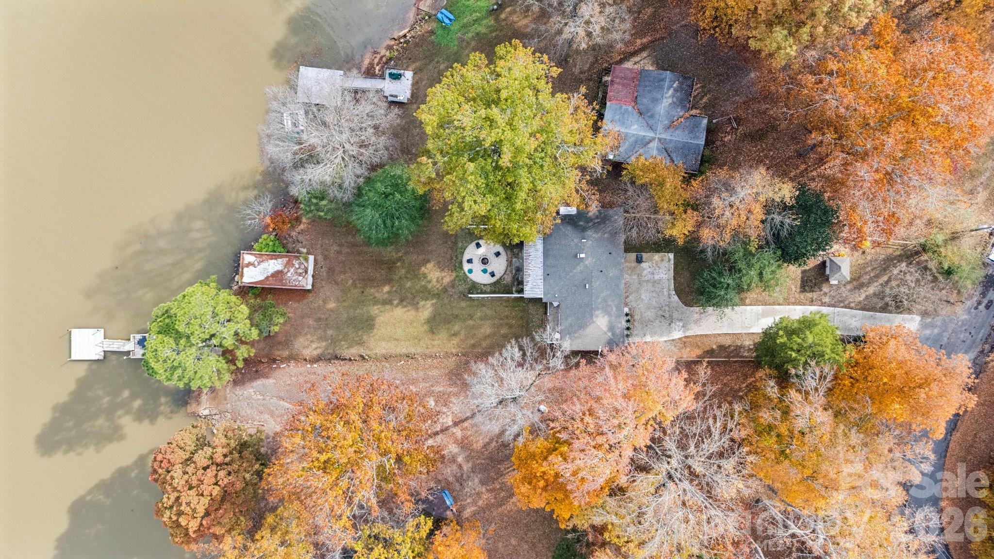 Aerial view of a lakeside home with two docks, a long driveway, and autumn trees.