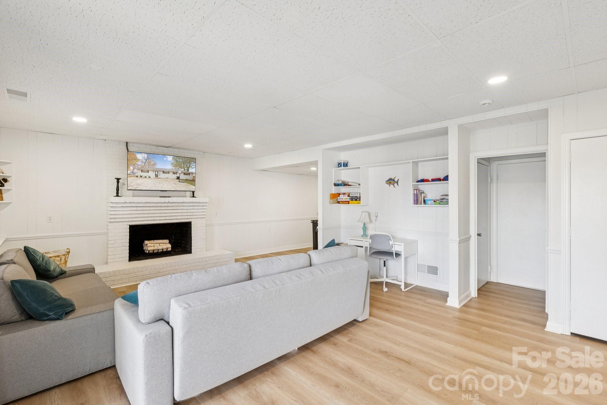 Living room with a white brick fireplace, gray sectional sofas, built-in shelves, and light wood flooring.