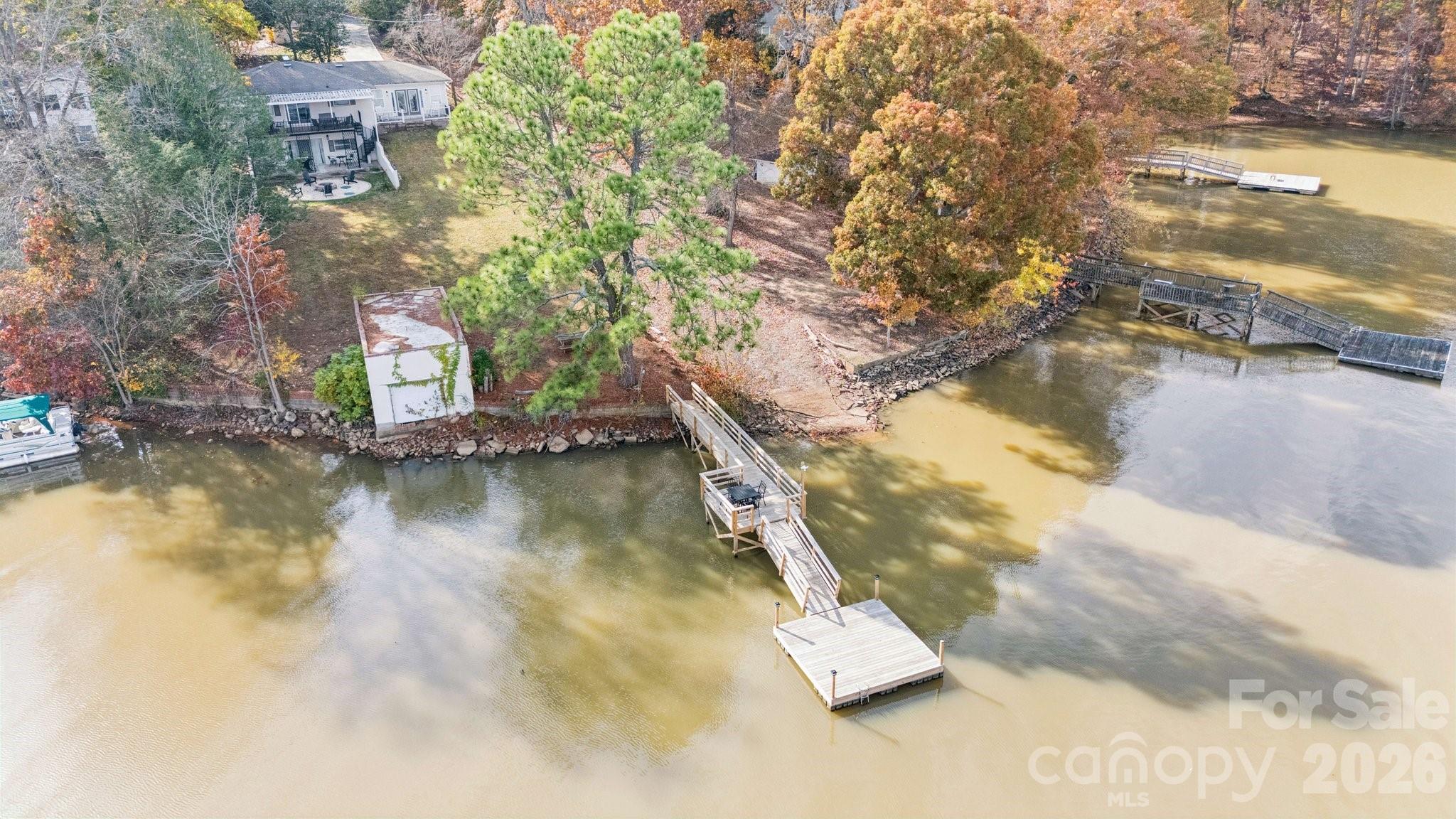 Aerial view of lakeside home, wooded shoreline, multiple docks, and private pier.
