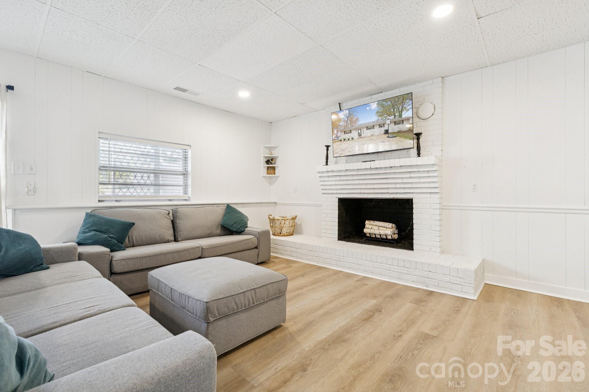 Living room with a gray sectional and white brick fireplace beneath a television.