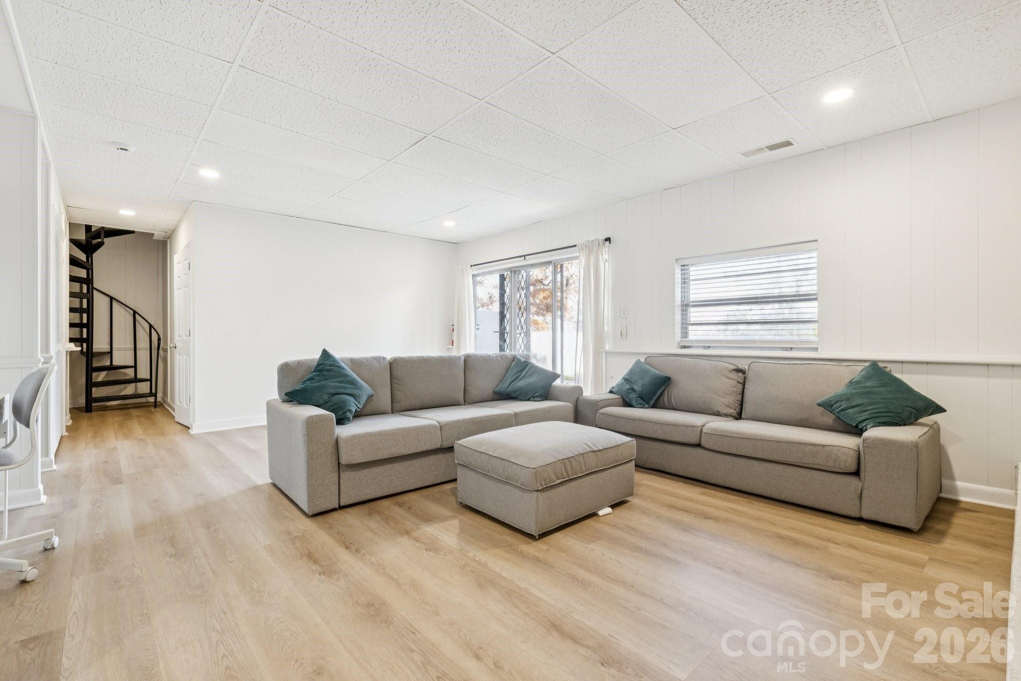 Living room with gray sectional sofas, teal pillows, and a black spiral staircase.