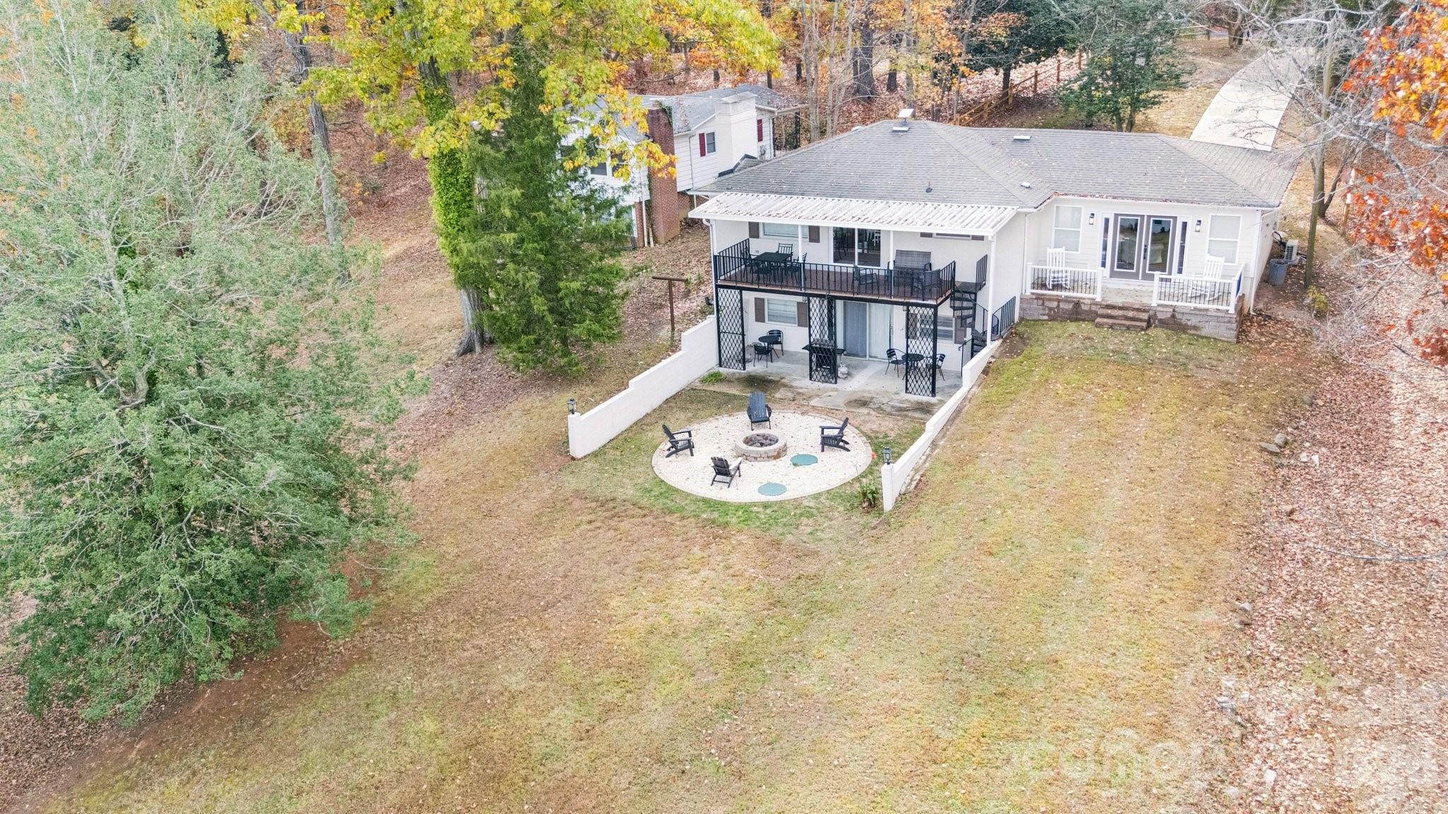 Aerial view of a white home’s backyard, with an elevated deck and circular fire pit seating area.