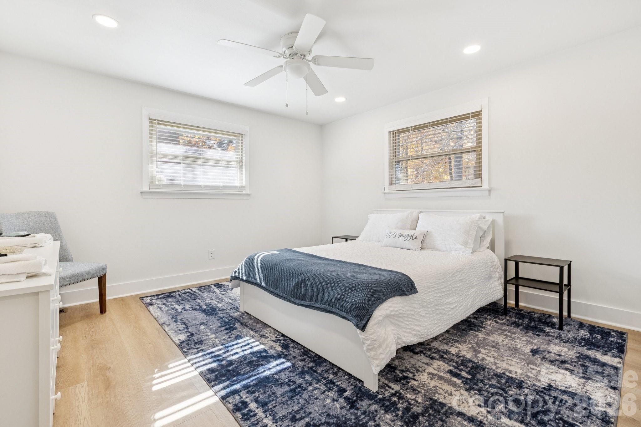 Furnished bedroom with a white bed, navy throw, patterned rug, and ceiling fan.