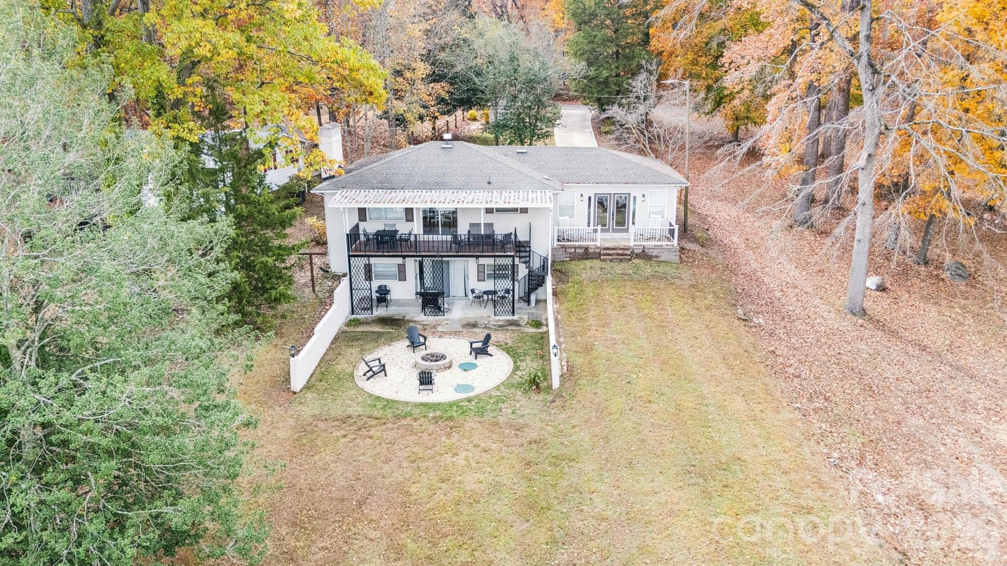 Aerial view of a wooded home with outdoor decks and a circular fire-pit seating area.