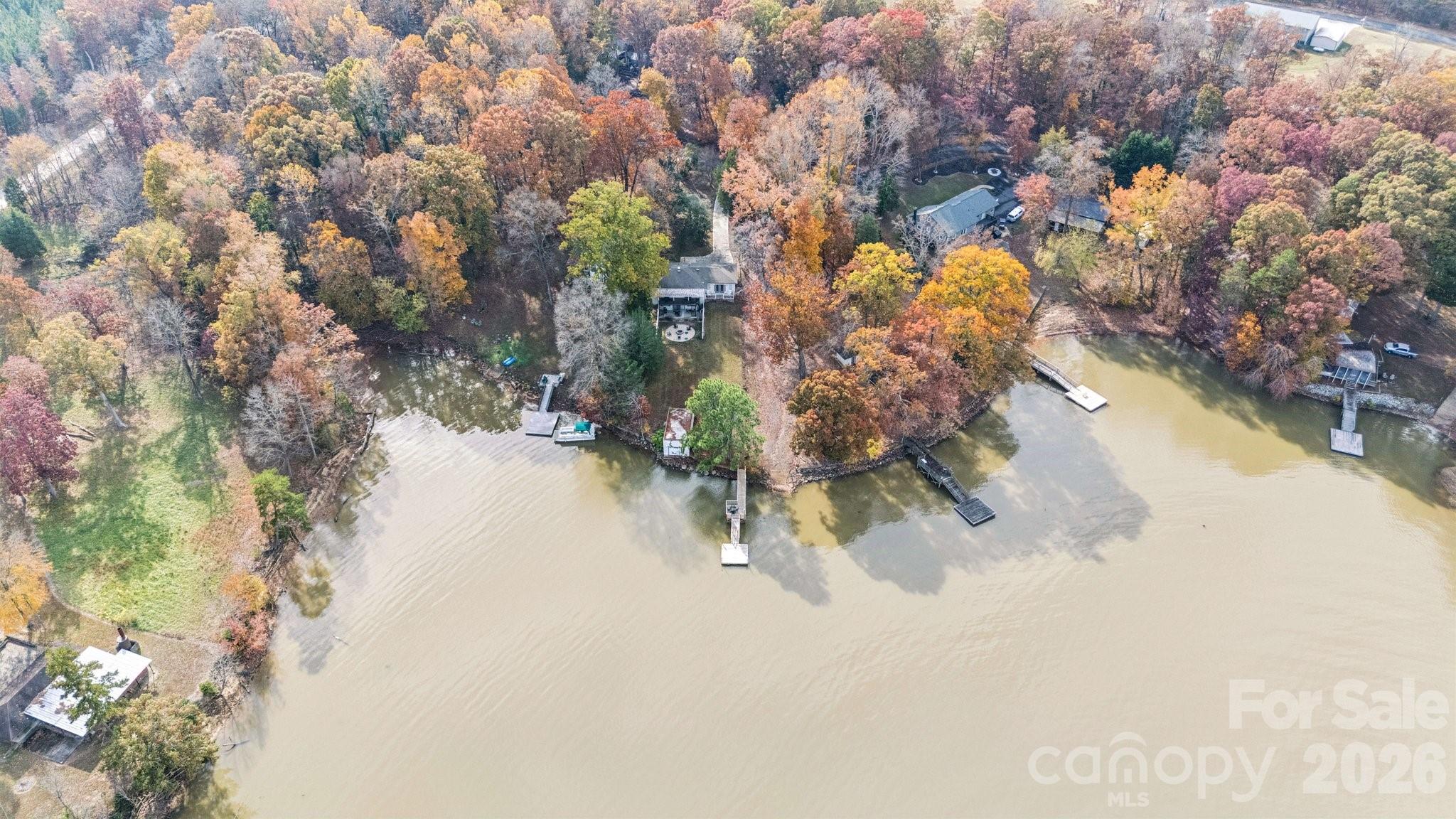 Wooded waterfront home with a private dock extending into the lake, viewed from above in autumn.