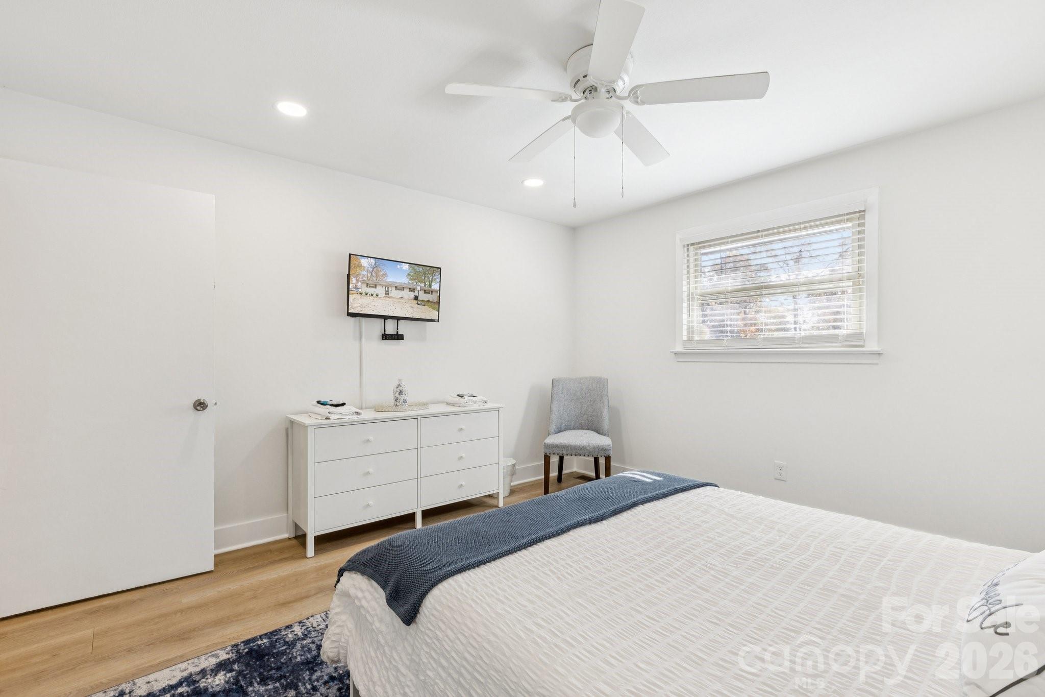 Furnished bedroom with a white dresser, gray chair, ceiling fan, and bed with a dark blue throw.