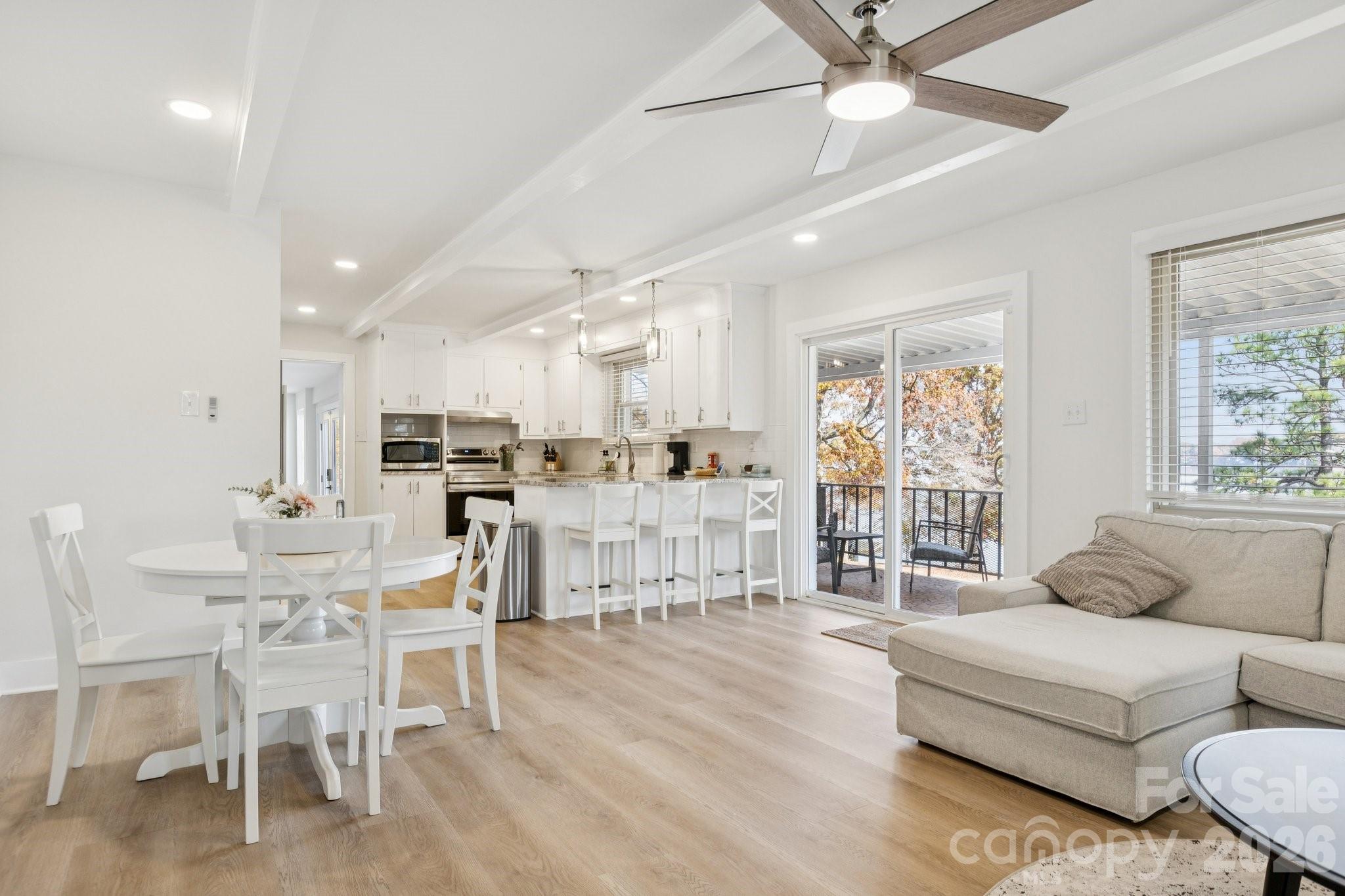Open-plan living room with white kitchen and dining area, wood floors, and sliding doors to a deck.
