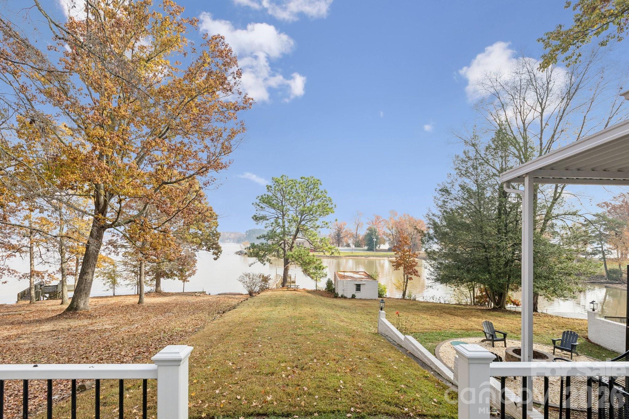 Lakefront backyard with a covered patio, grassy slope, and autumn trees.
