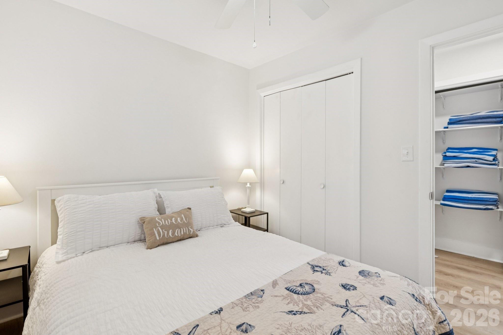 Bedroom with white bedding, a seashell-patterned blanket, and an open closet stocked with blue towels.