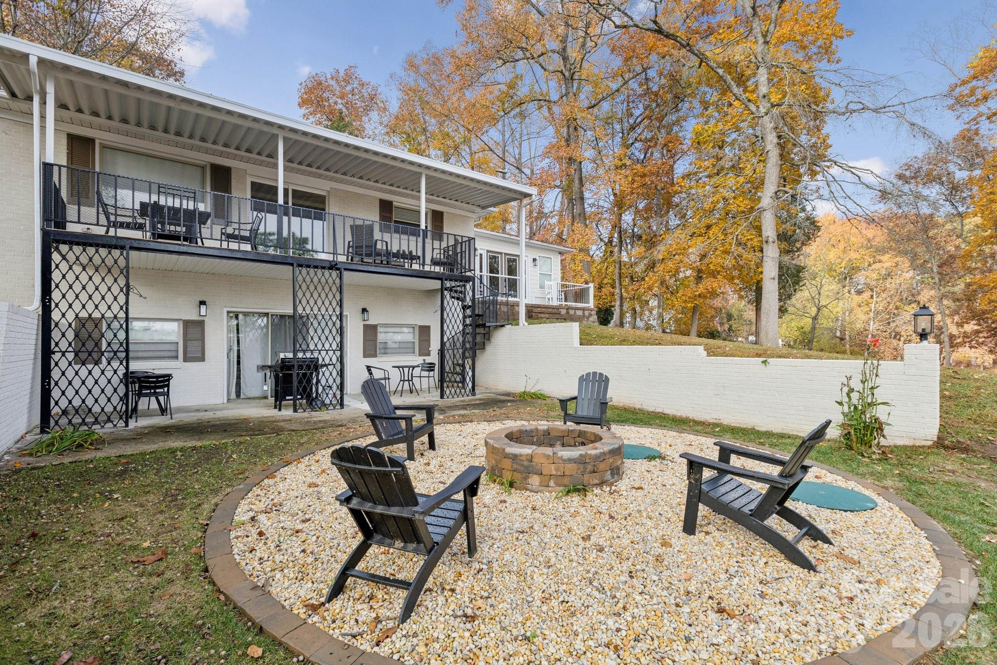 White-brick home with a raised deck and gravel fire-pit seating area in the backyard.