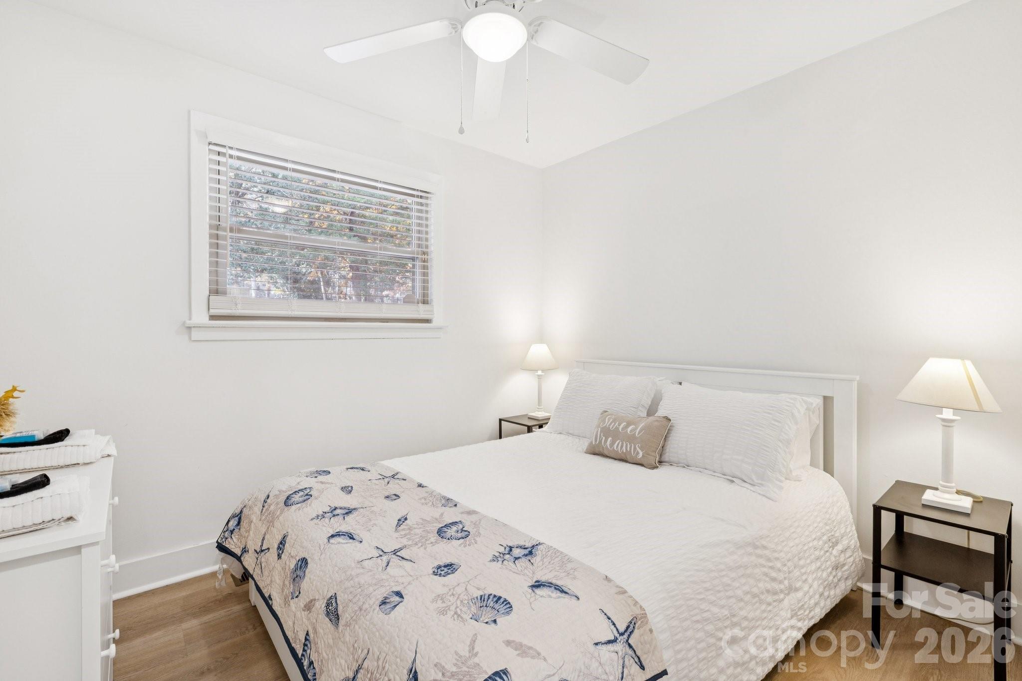 Bright bedroom with a white bed, shell-patterned quilt, and window with blinds.