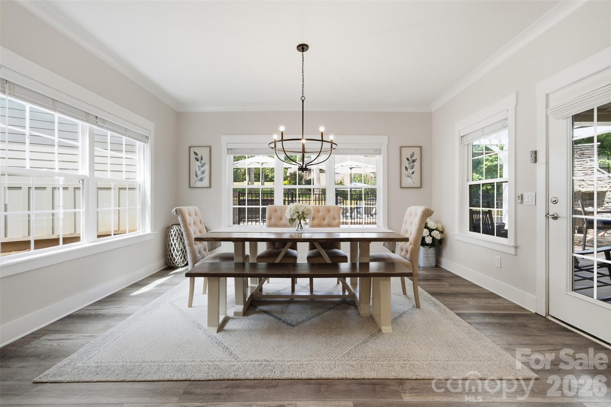Dining room with a dark-wood table, upholstered seating, chandelier, and large windows overlooking a patio.