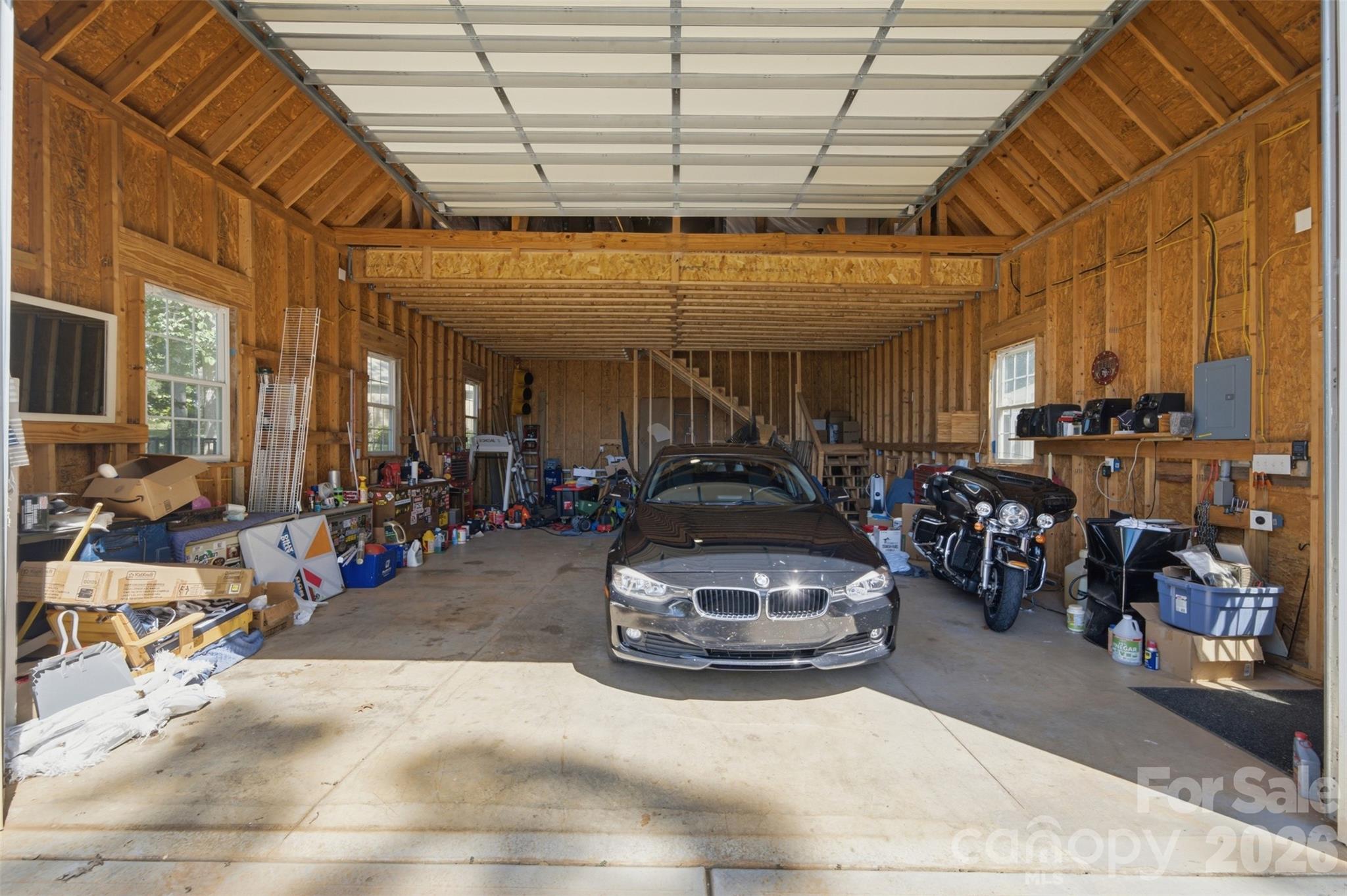 Large unfinished garage with exposed wood framing, a car in the center, and a motorcycle along the right wall.