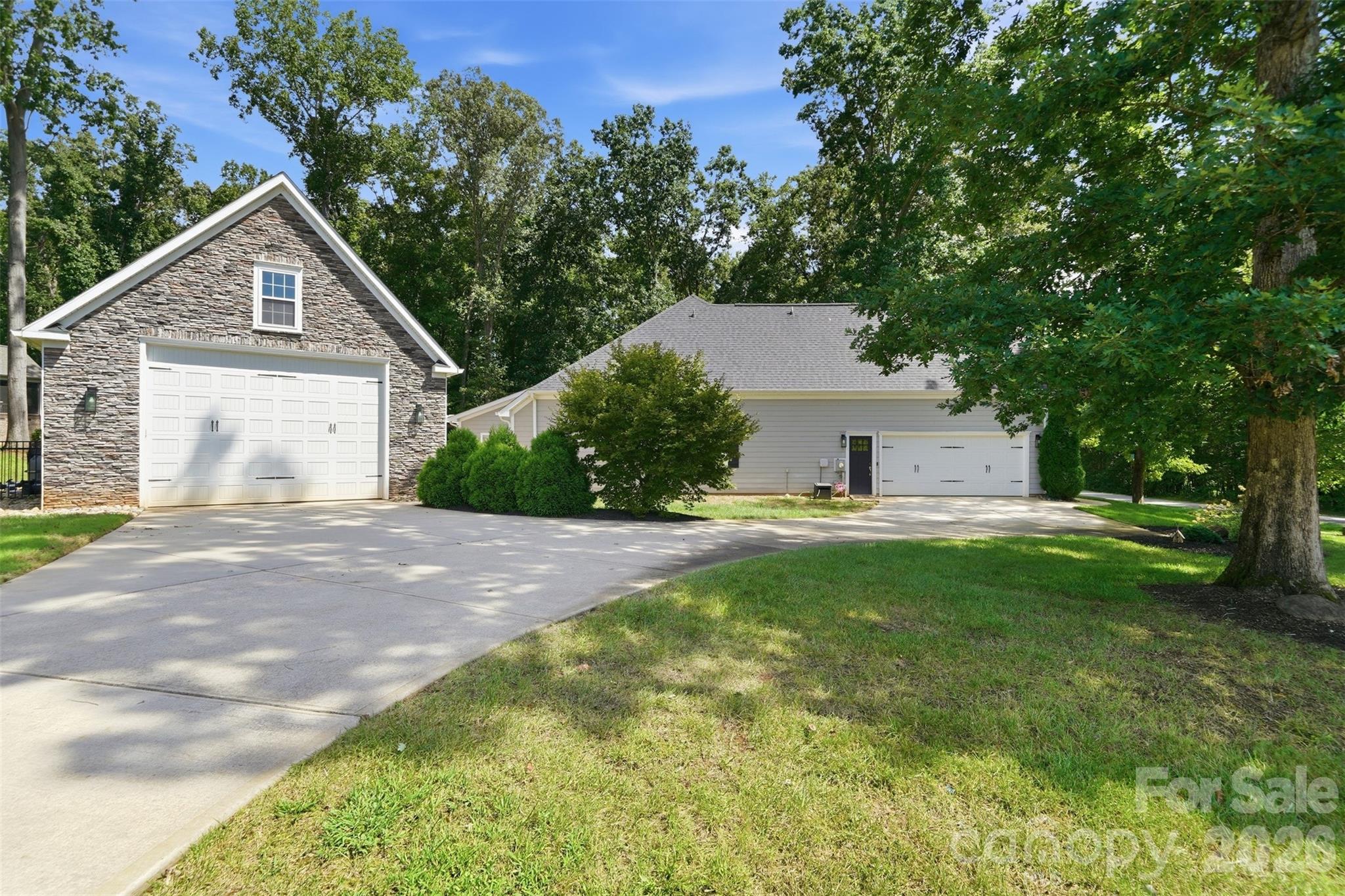Home exterior with a stone-faced gabled garage, a second garage, and a wide concrete driveway.