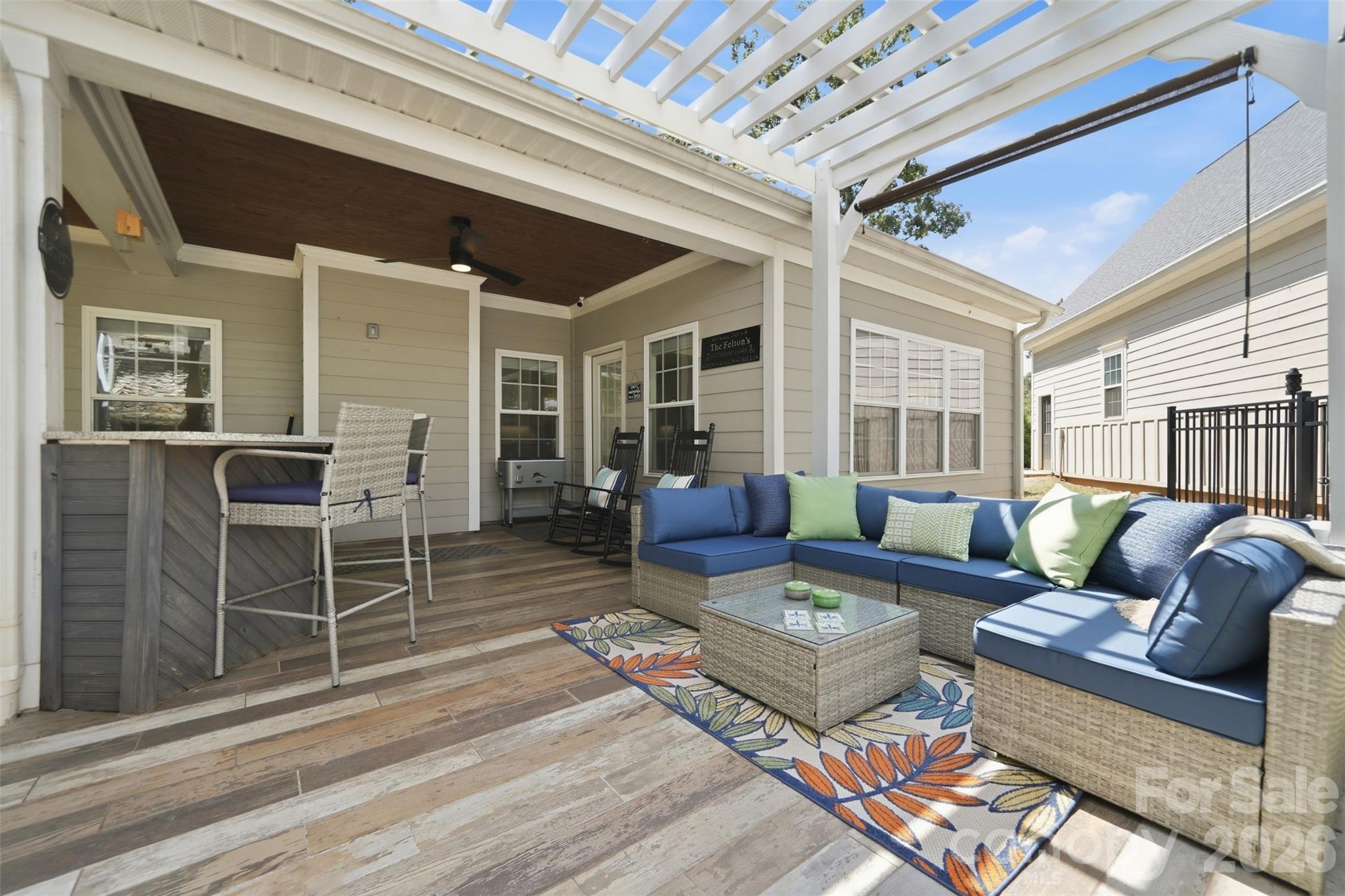 Covered patio with pergola, blue-cushioned sectional, bar counter, and wood-look tile flooring.