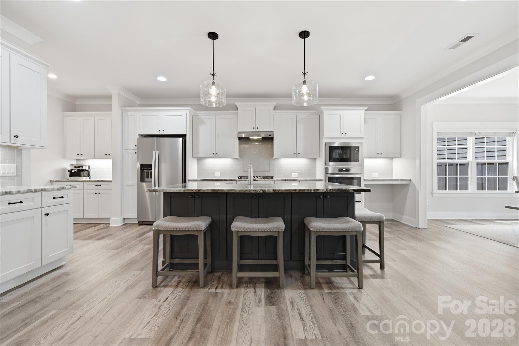 Bright kitchen with a large dark island, white cabinetry, stainless steel appliances, and three stools.