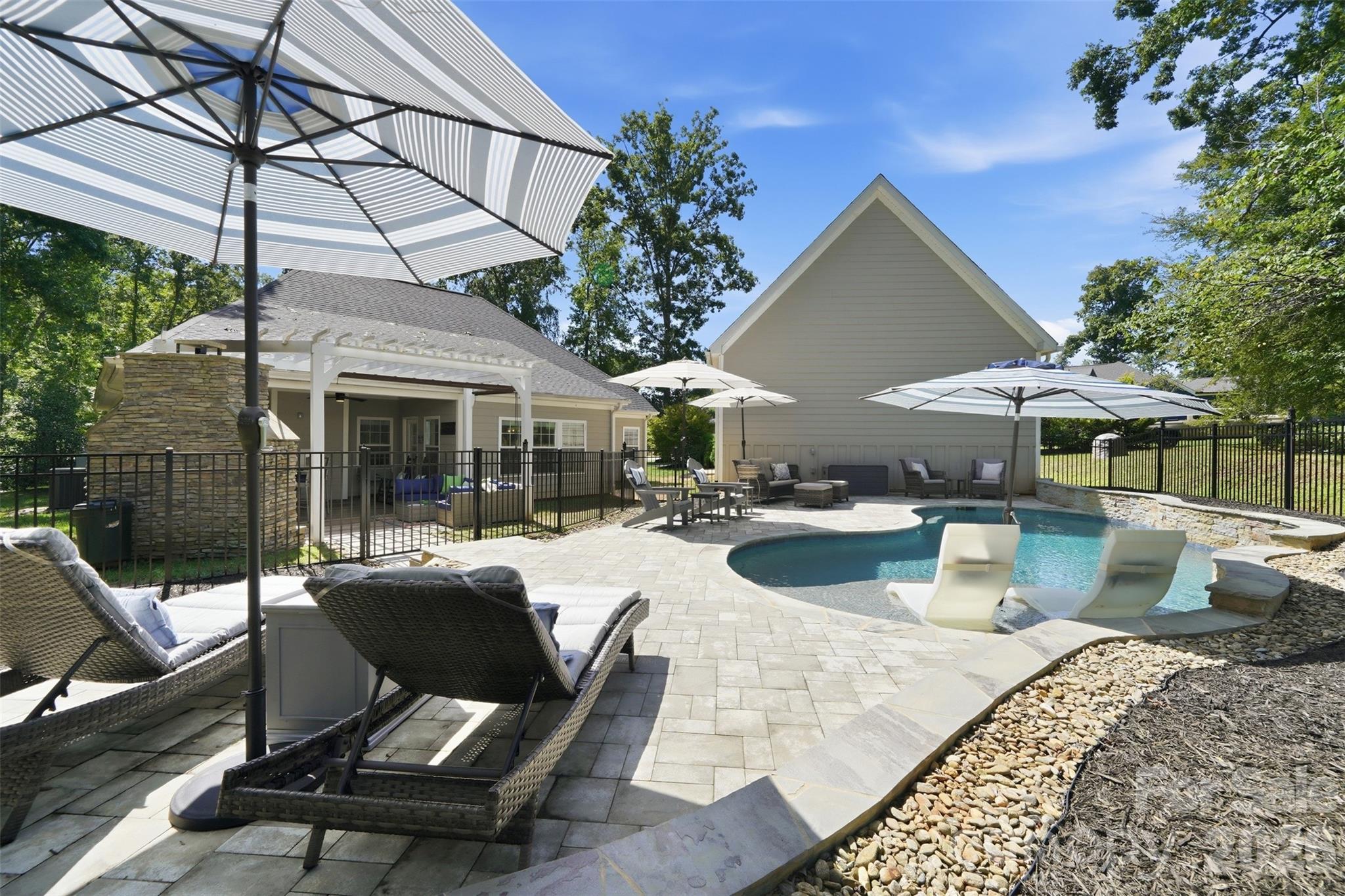 Backyard pool and paved patio with striped umbrellas, lounge seating, and a covered pergola.
