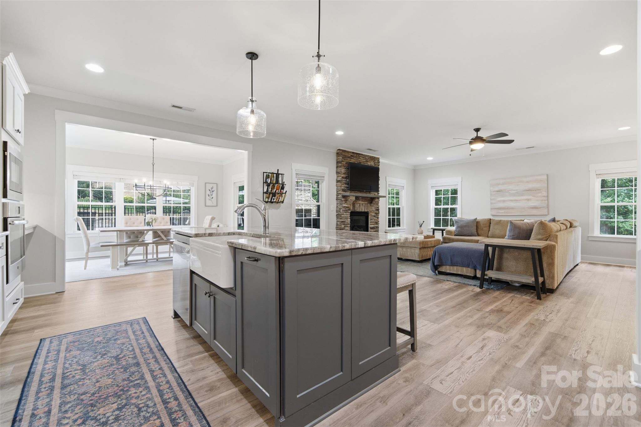 Open-plan kitchen with a large gray island, dining area, and living room with a stone fireplace.