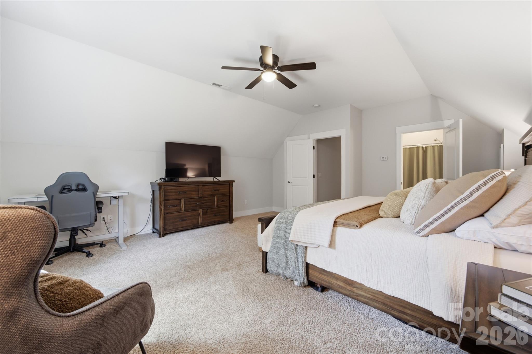 Furnished bedroom with a sloped ceiling, neutral bedding, and a desk beside the bed.