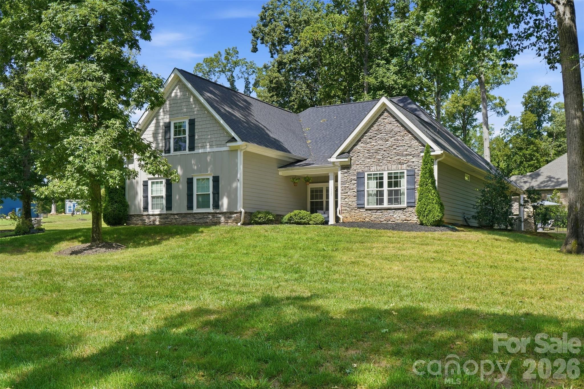 Gray-green two-story home with a stone-front gable, broad lawn, and mature shade trees.