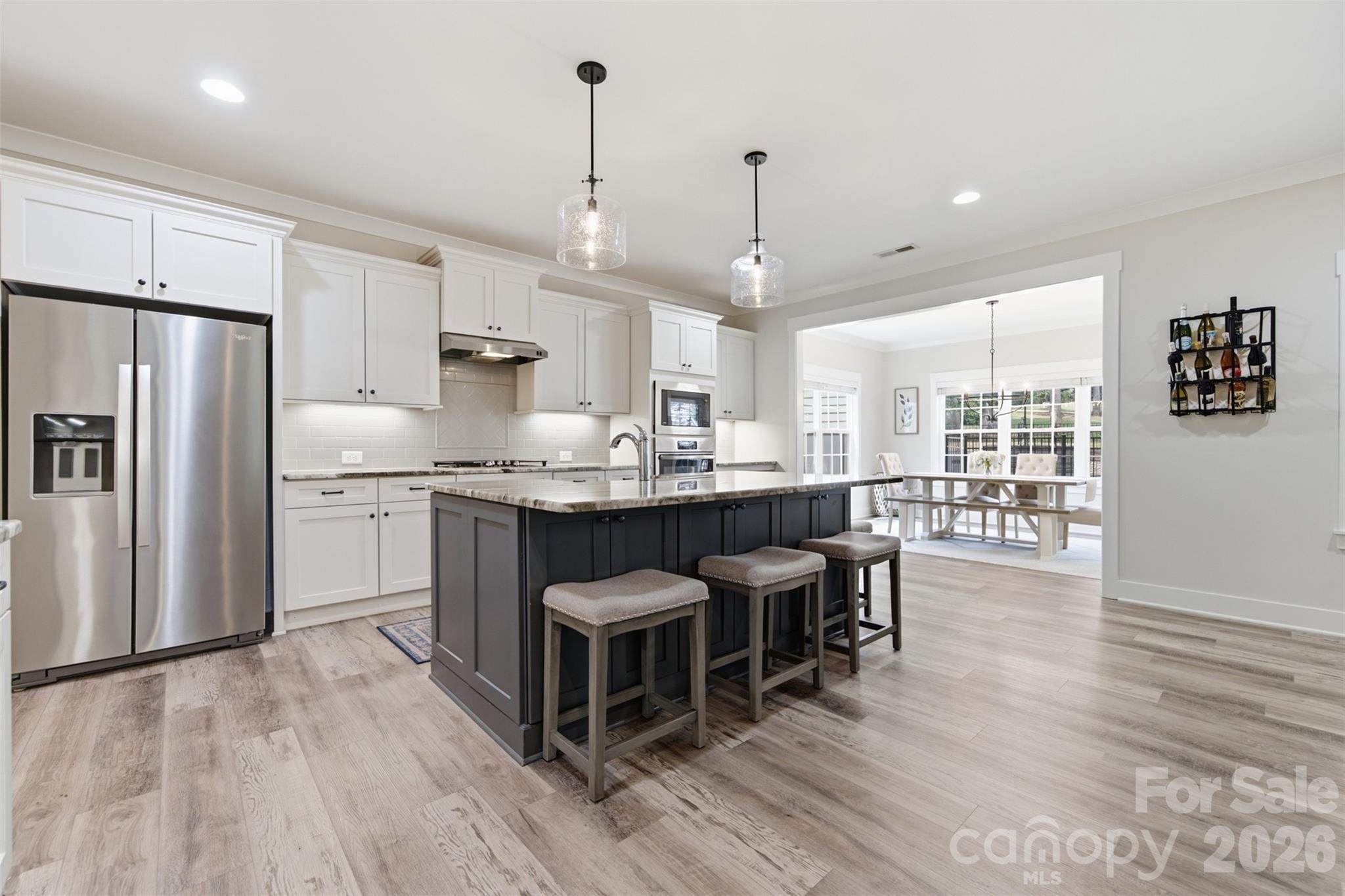 Open-plan kitchen with white cabinets, stainless appliances, dark island, and adjoining bright dining area.
