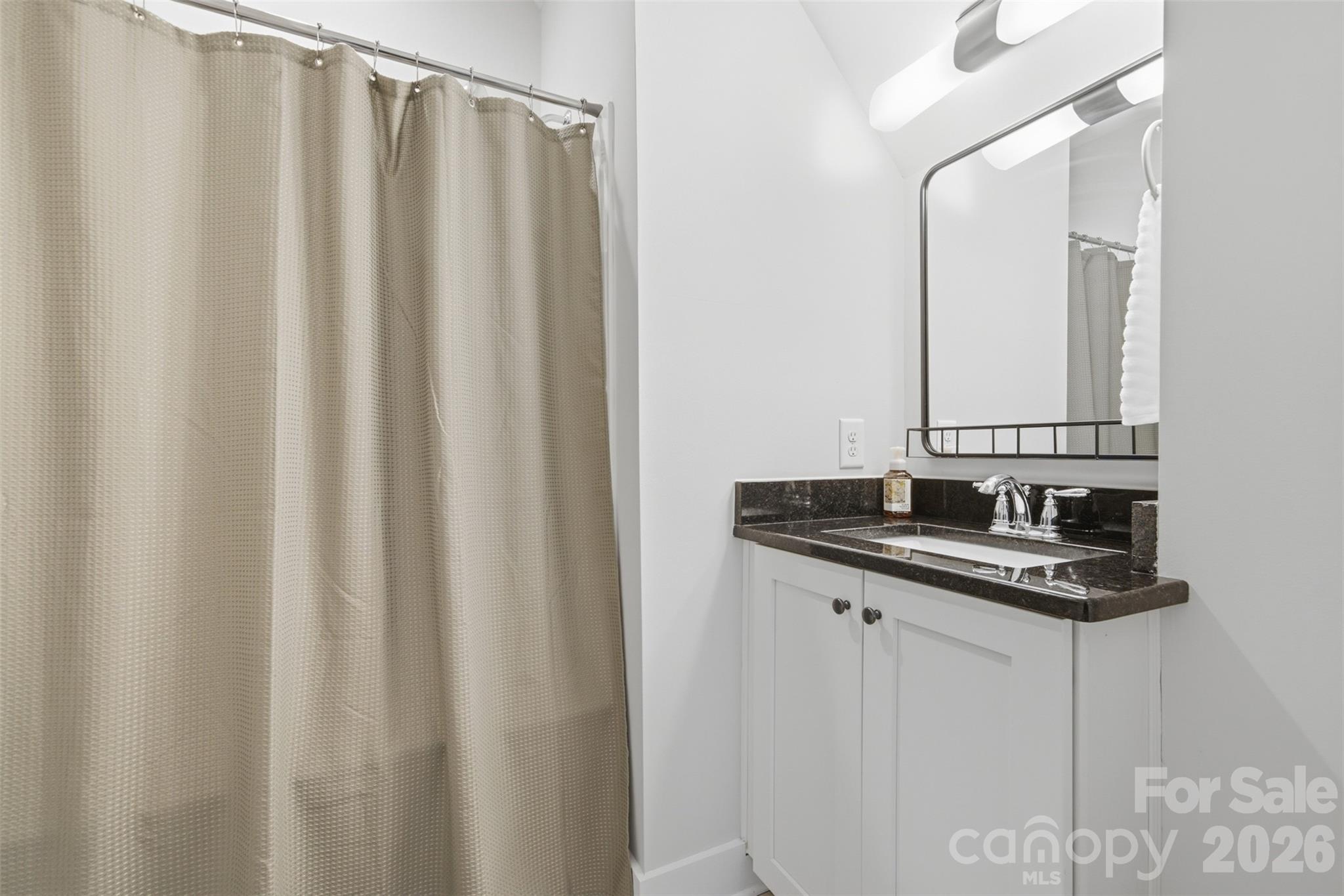 Bathroom vanity with dark granite countertop, large mirror, and beige shower curtain.