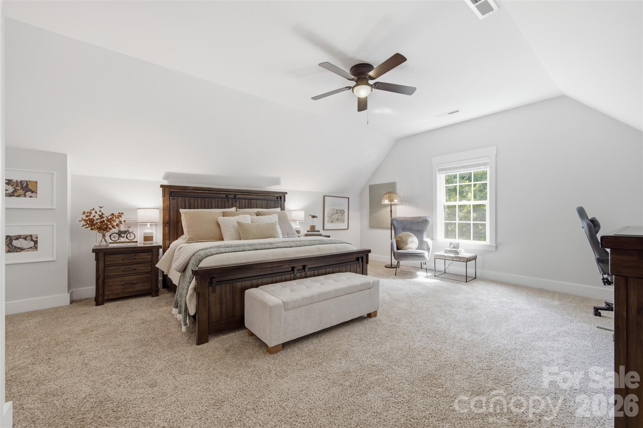 Furnished bedroom with a dark wood bed, high sloped ceiling, and bright window-side sitting area.