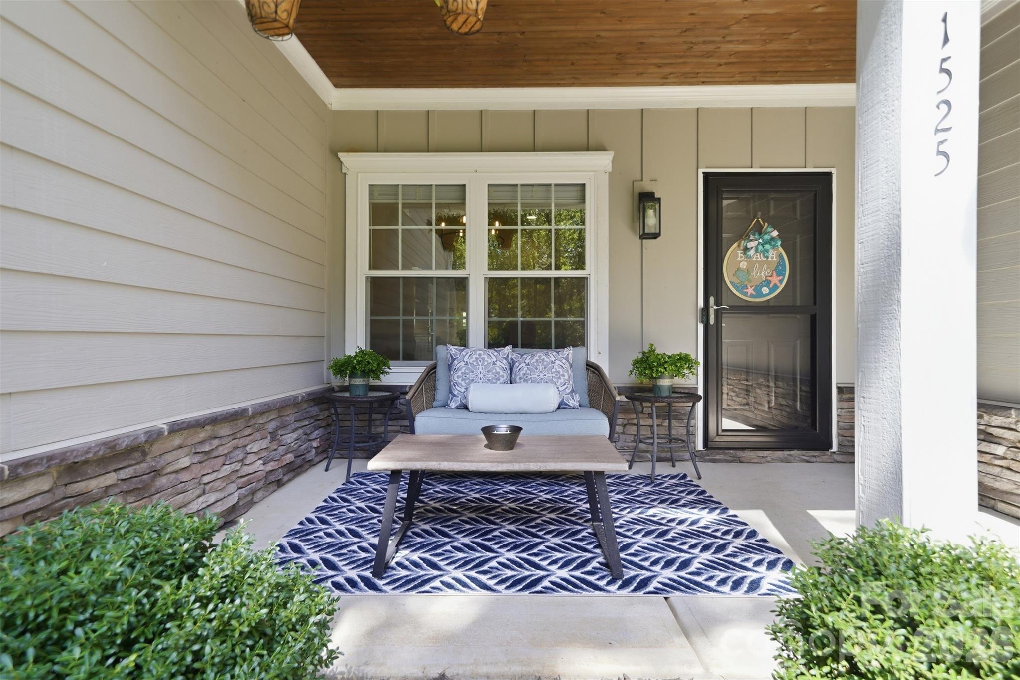 Covered front porch with cushioned loveseat, patterned rug, and wood-plank ceiling.