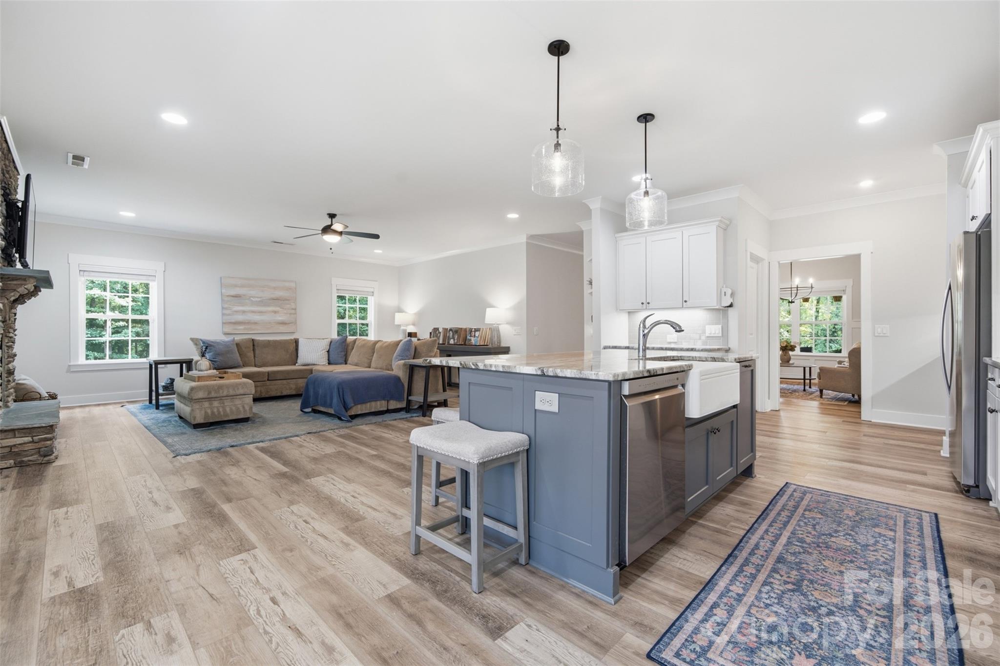 Open-plan kitchen and living room with a blue island, sectional sofa, and stone fireplace.