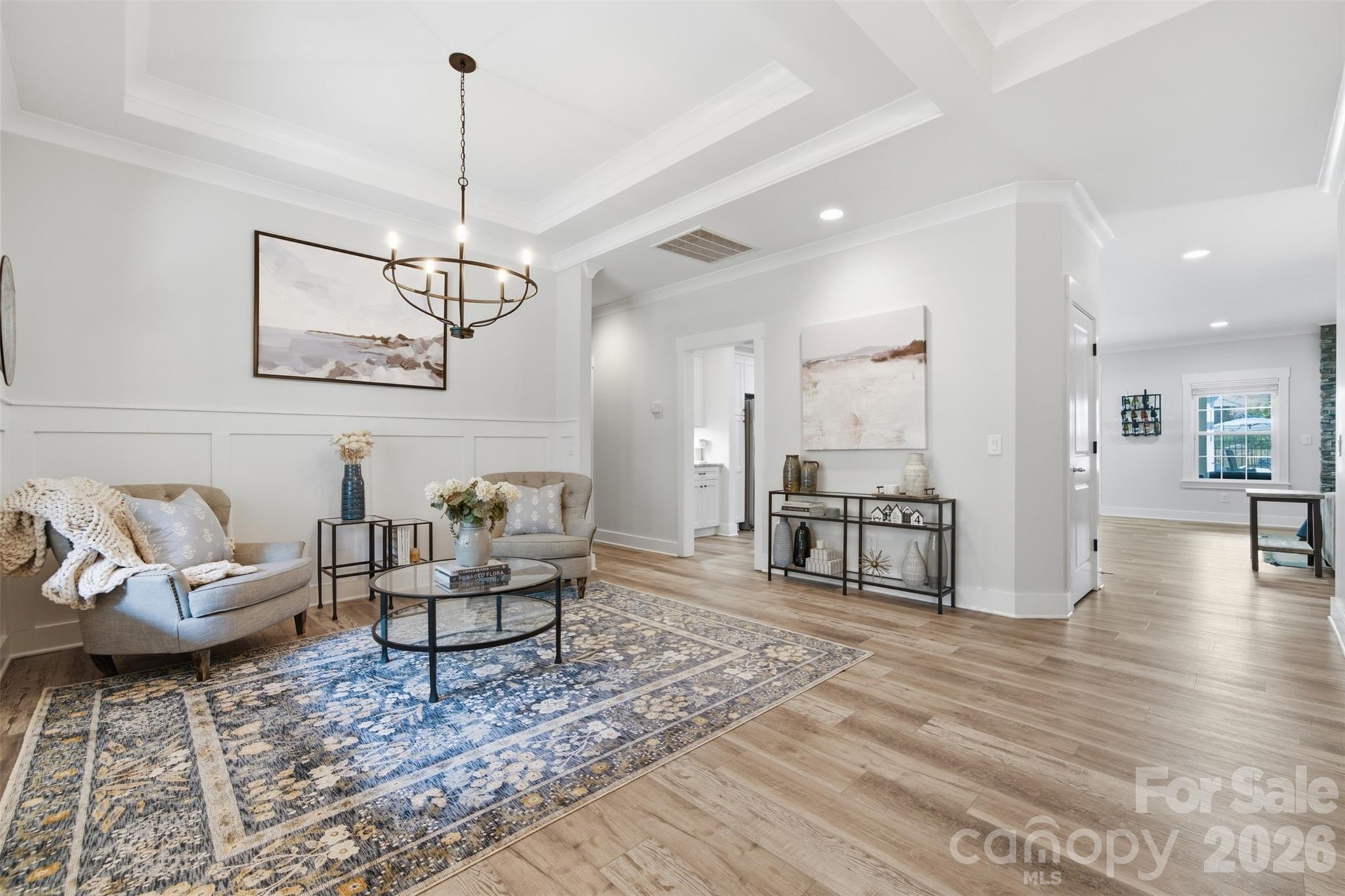 Staged living room with a blue patterned rug, paneled walls, and a dark metal chandelier.