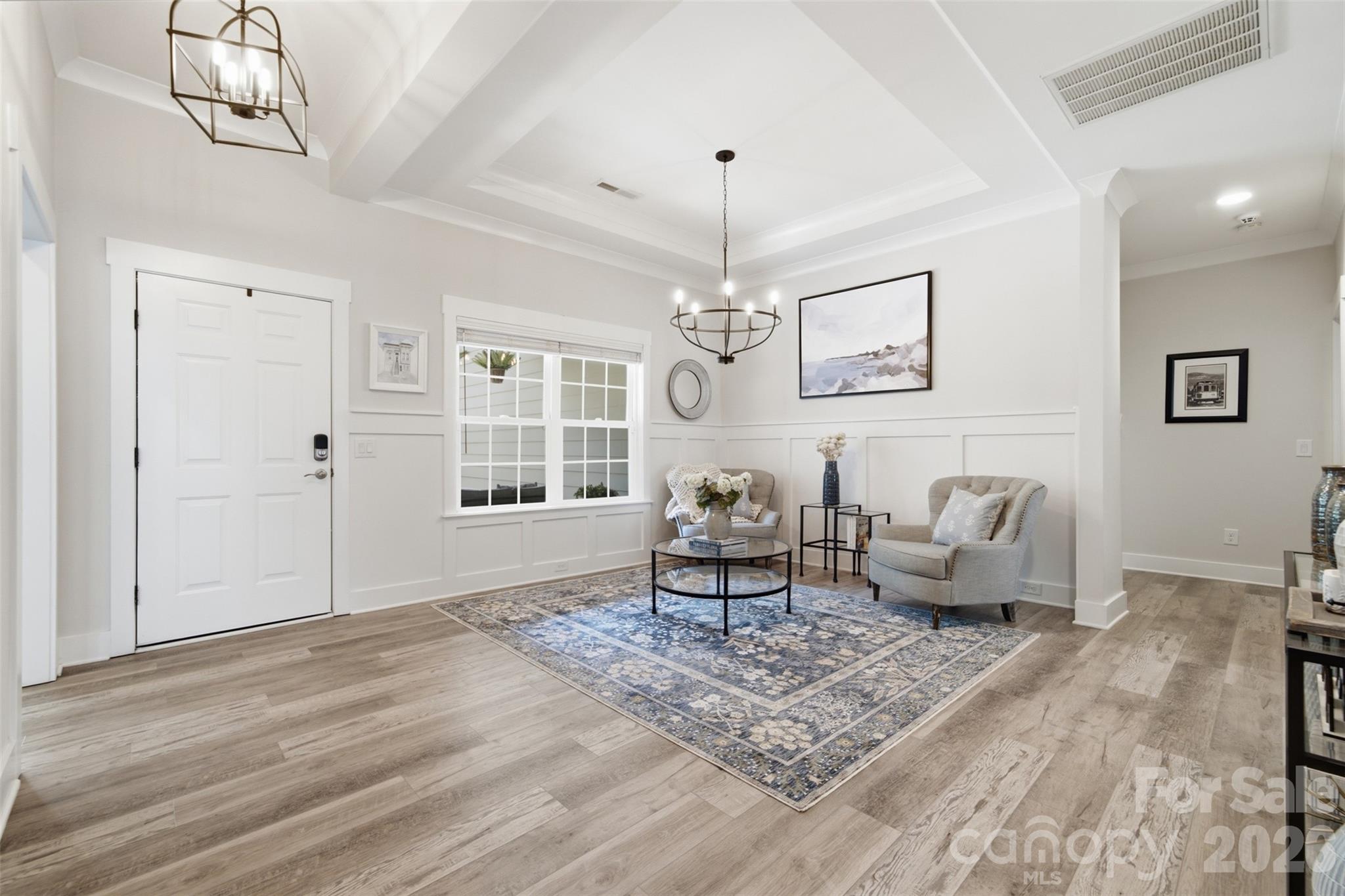 Staged entry sitting area with a white front door, tray ceiling, upholstered chairs, and blue patterned rug.