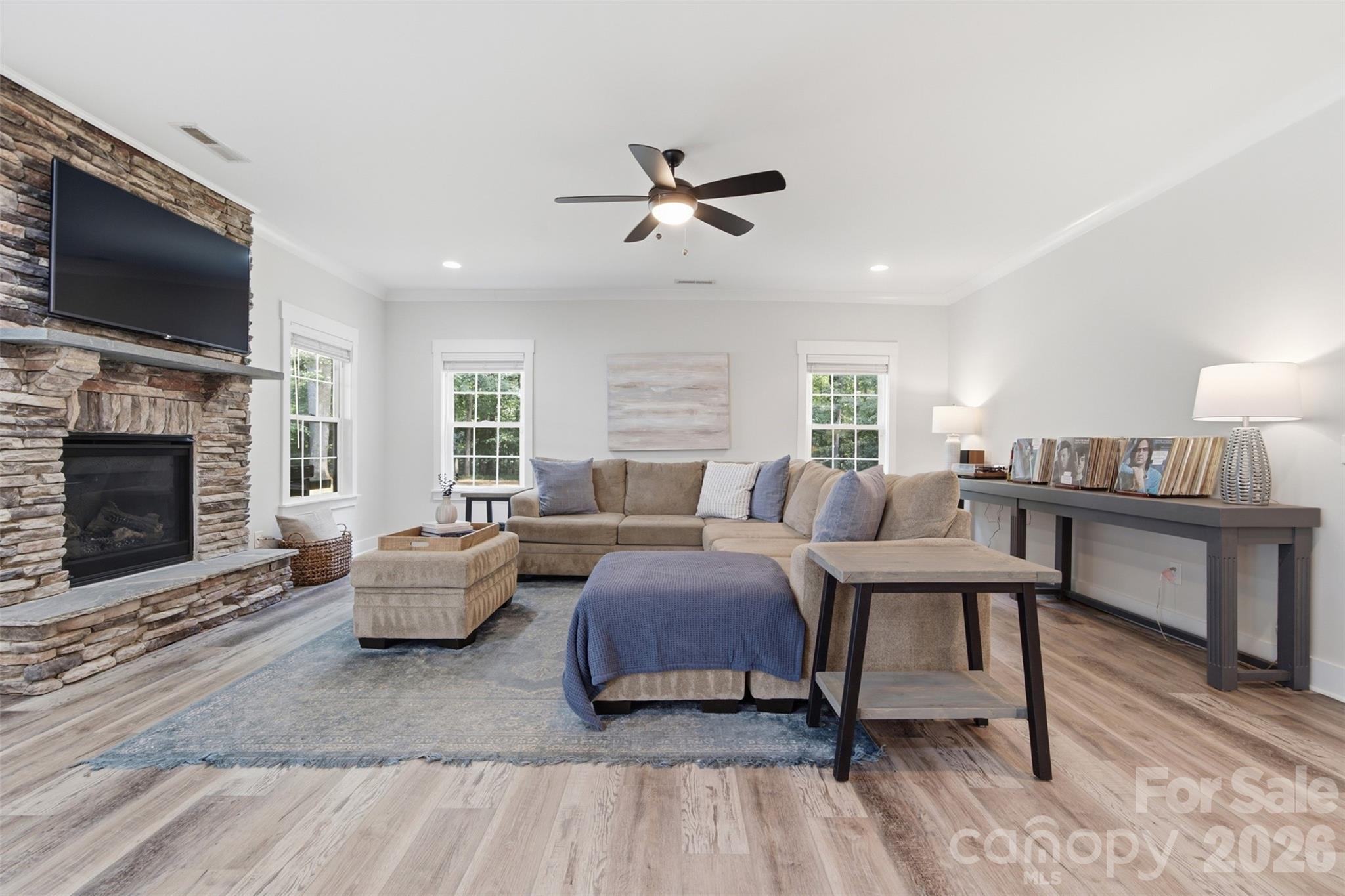 Furnished living room with a stone fireplace, mounted television, and beige sectional sofa.