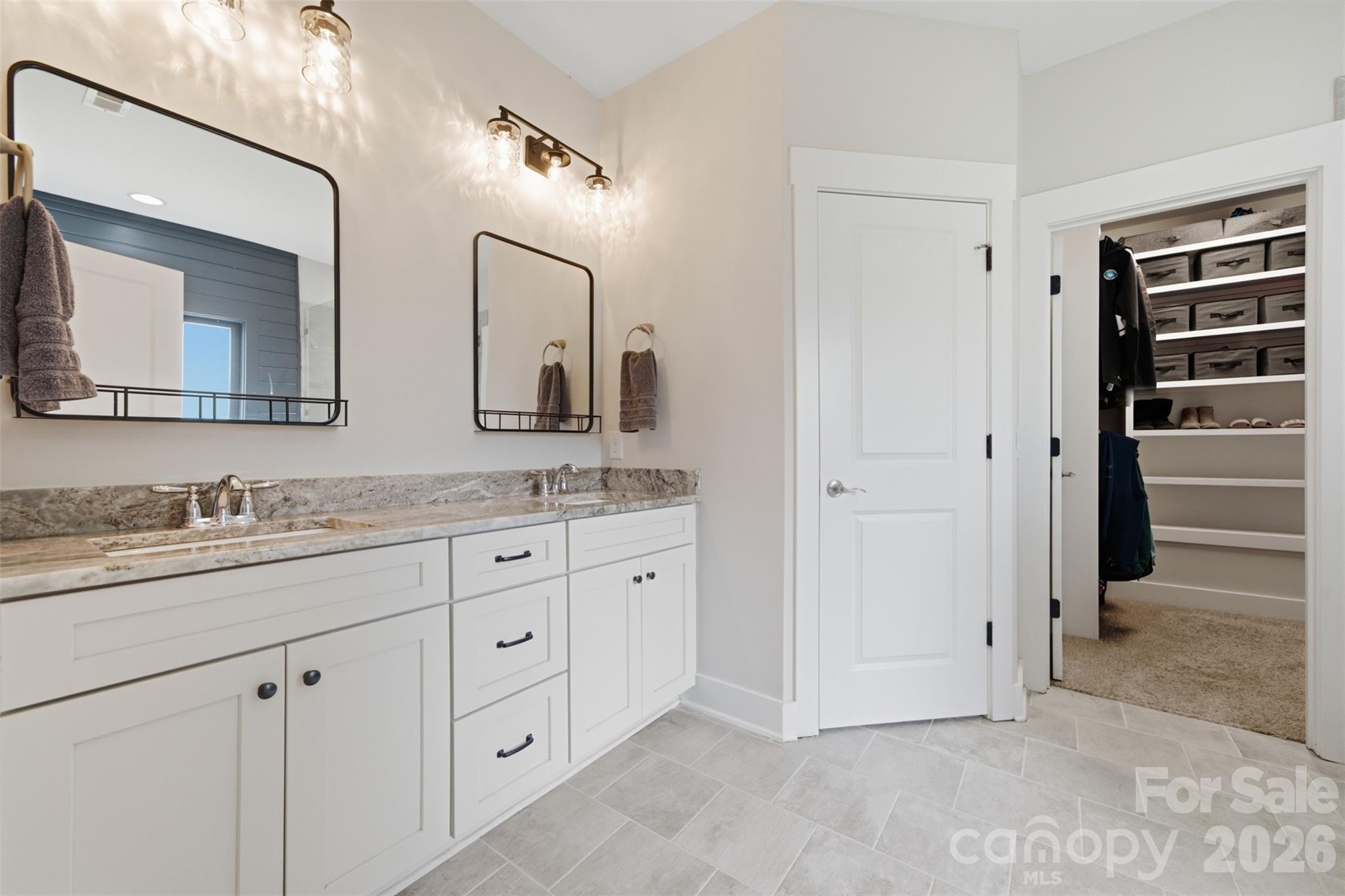 Bathroom with a long double vanity, stone counters, black-framed mirrors, and an open walk-in closet.