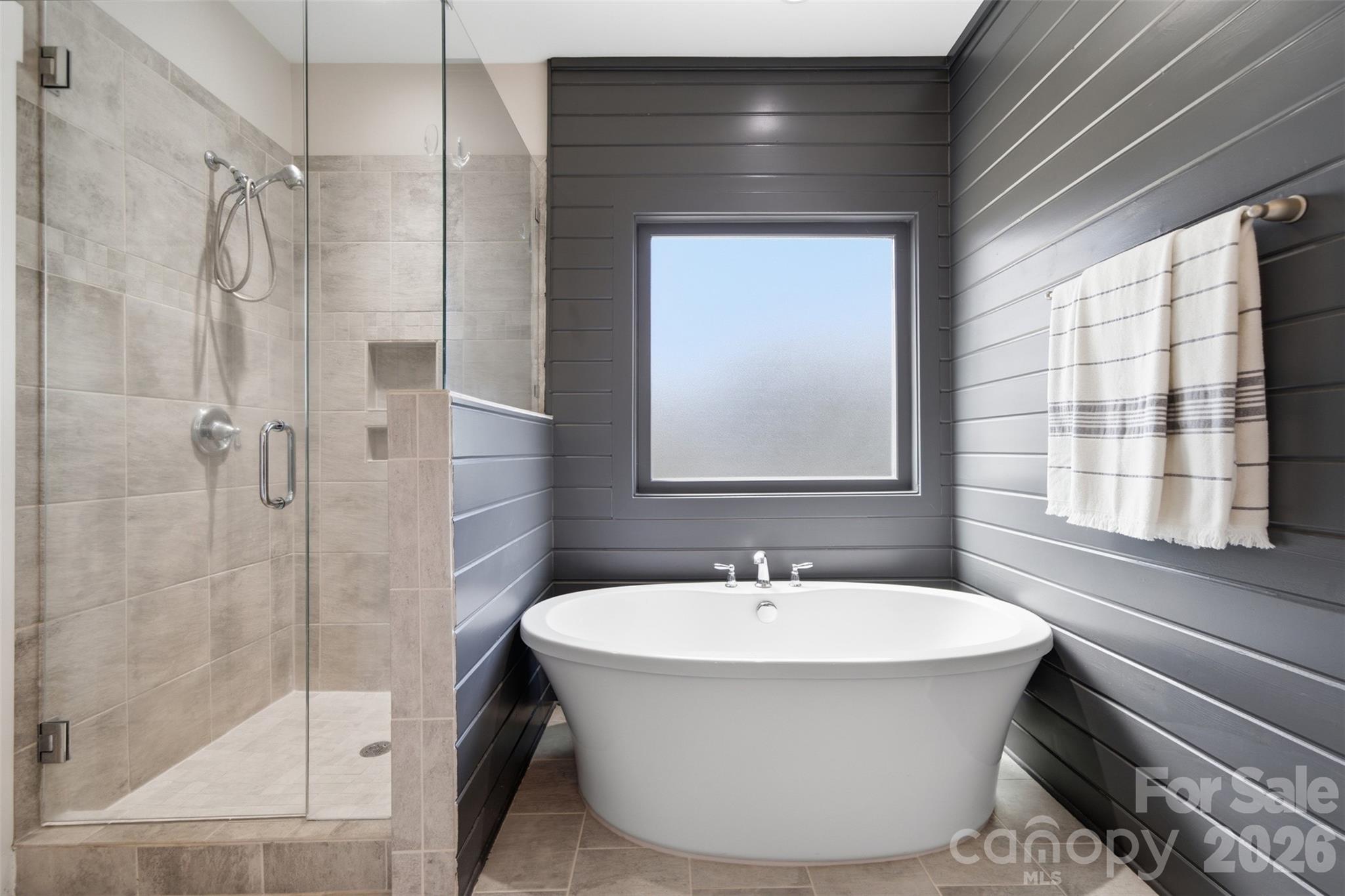 Modern bathroom with a freestanding tub beneath a frosted window and a glass-enclosed tiled shower.