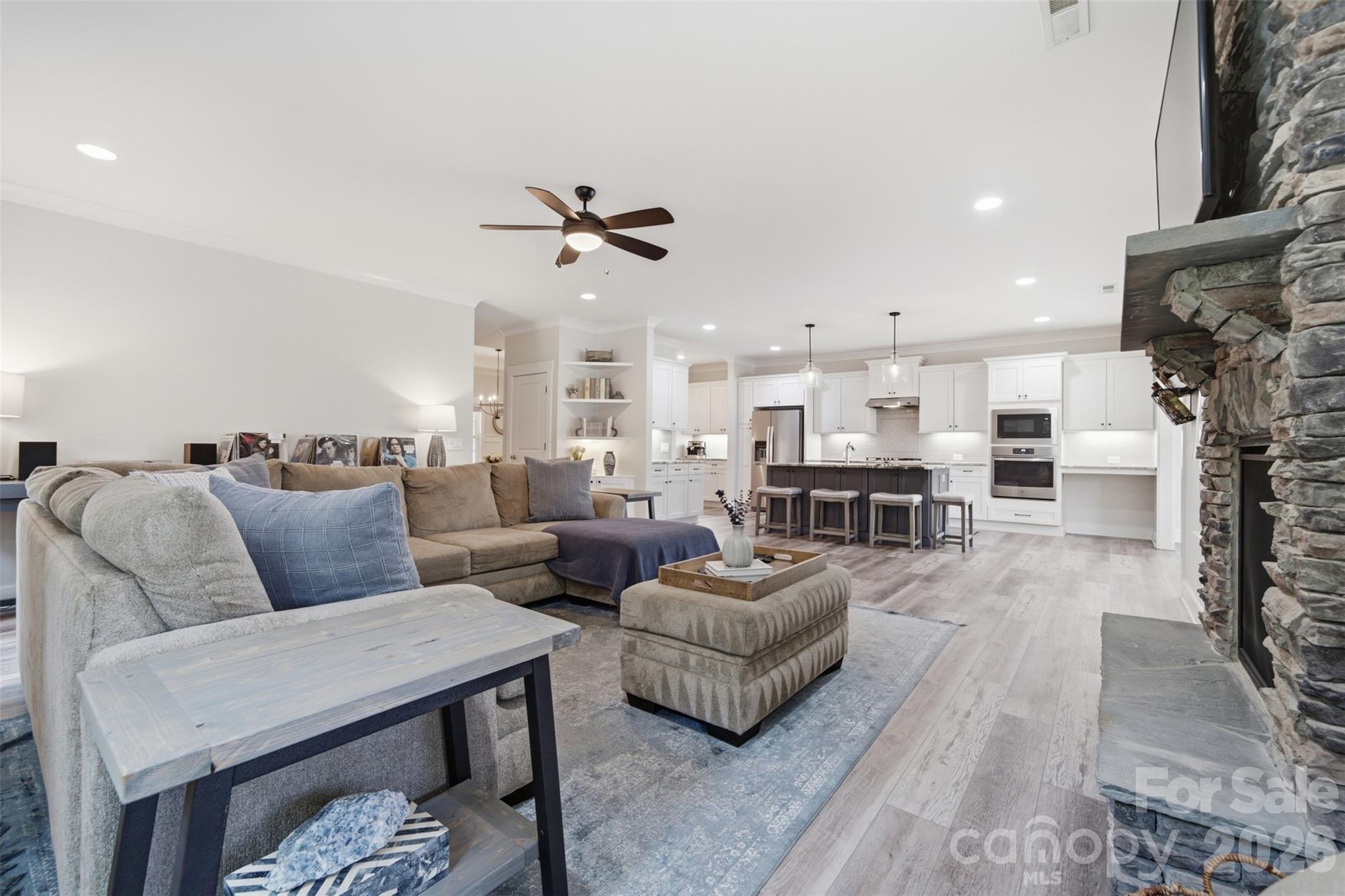 Open living room and kitchen with a sectional sofa, stone fireplace, and island with bar stools.