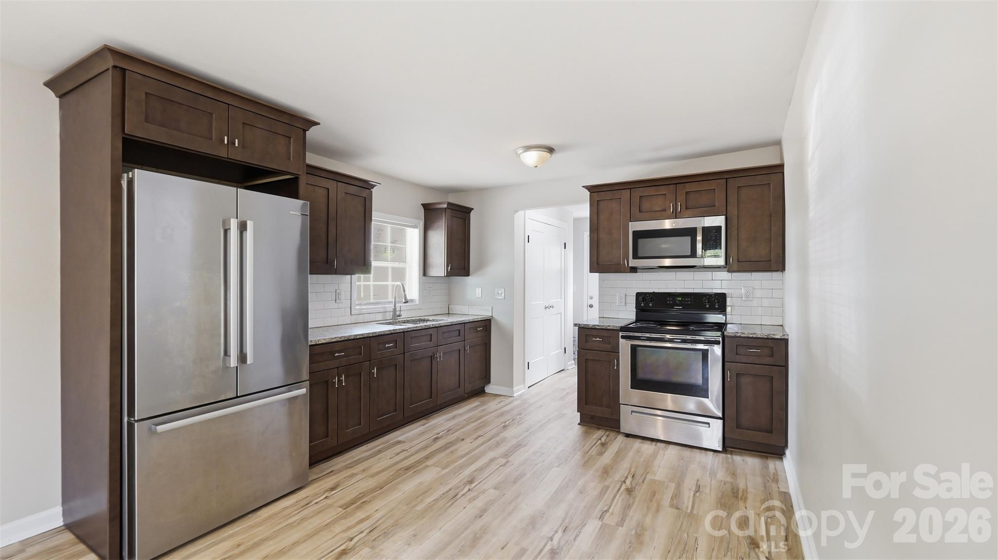 Kitchen with dark wood cabinets, stainless steel appliances, granite counters, and light wood-look flooring.