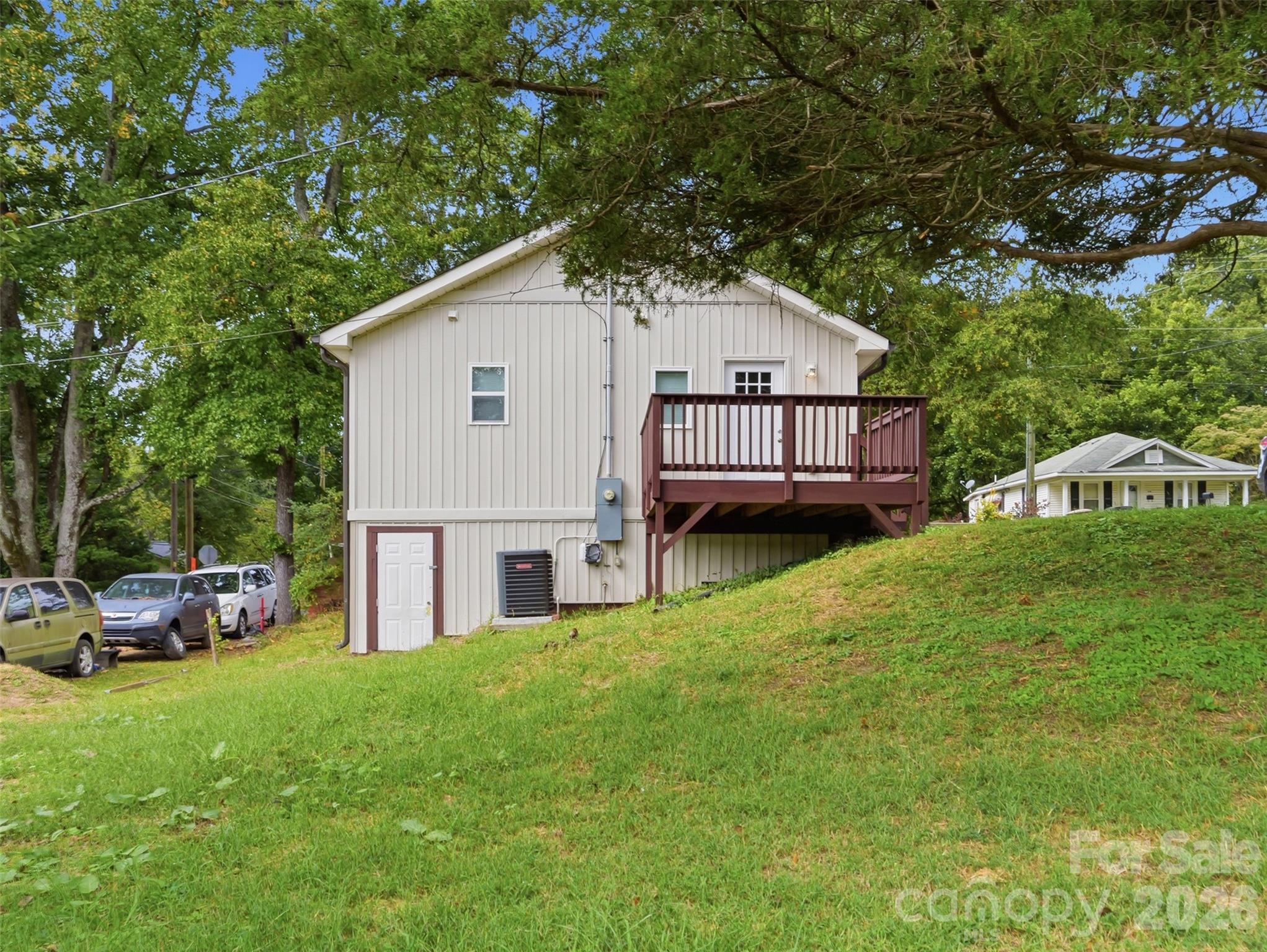 House exterior with a raised burgundy deck on a grassy slope beneath mature trees.