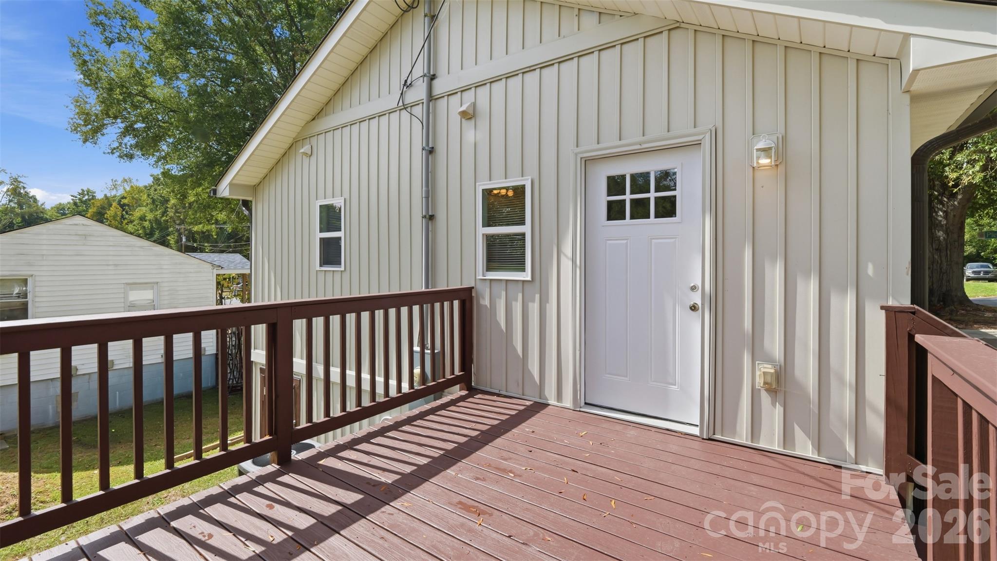 Raised wooden deck beside a light-sided home, with brown railings and a white entry door.
