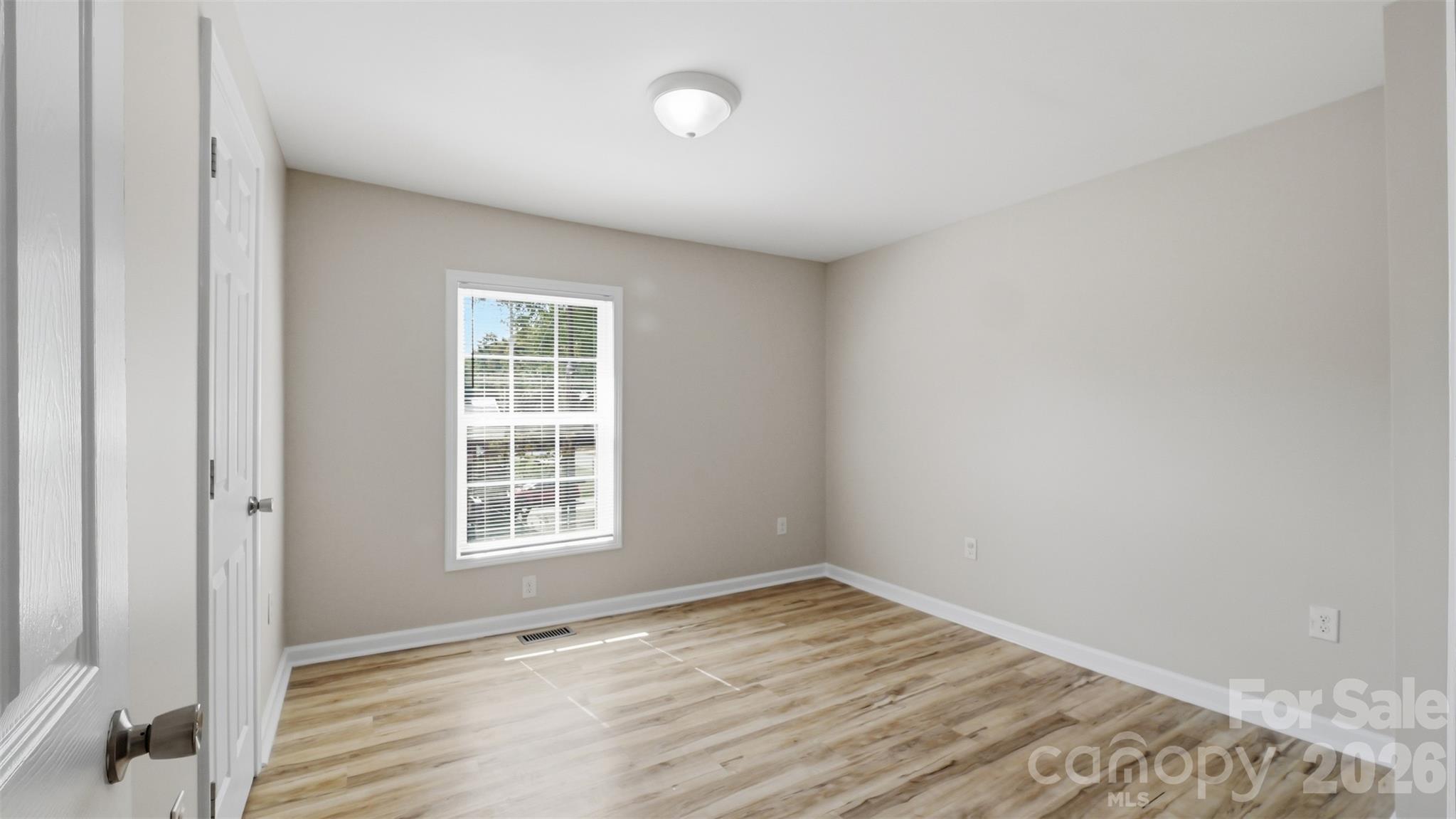 Empty room with wood-look flooring, gray walls, and a window with blinds.