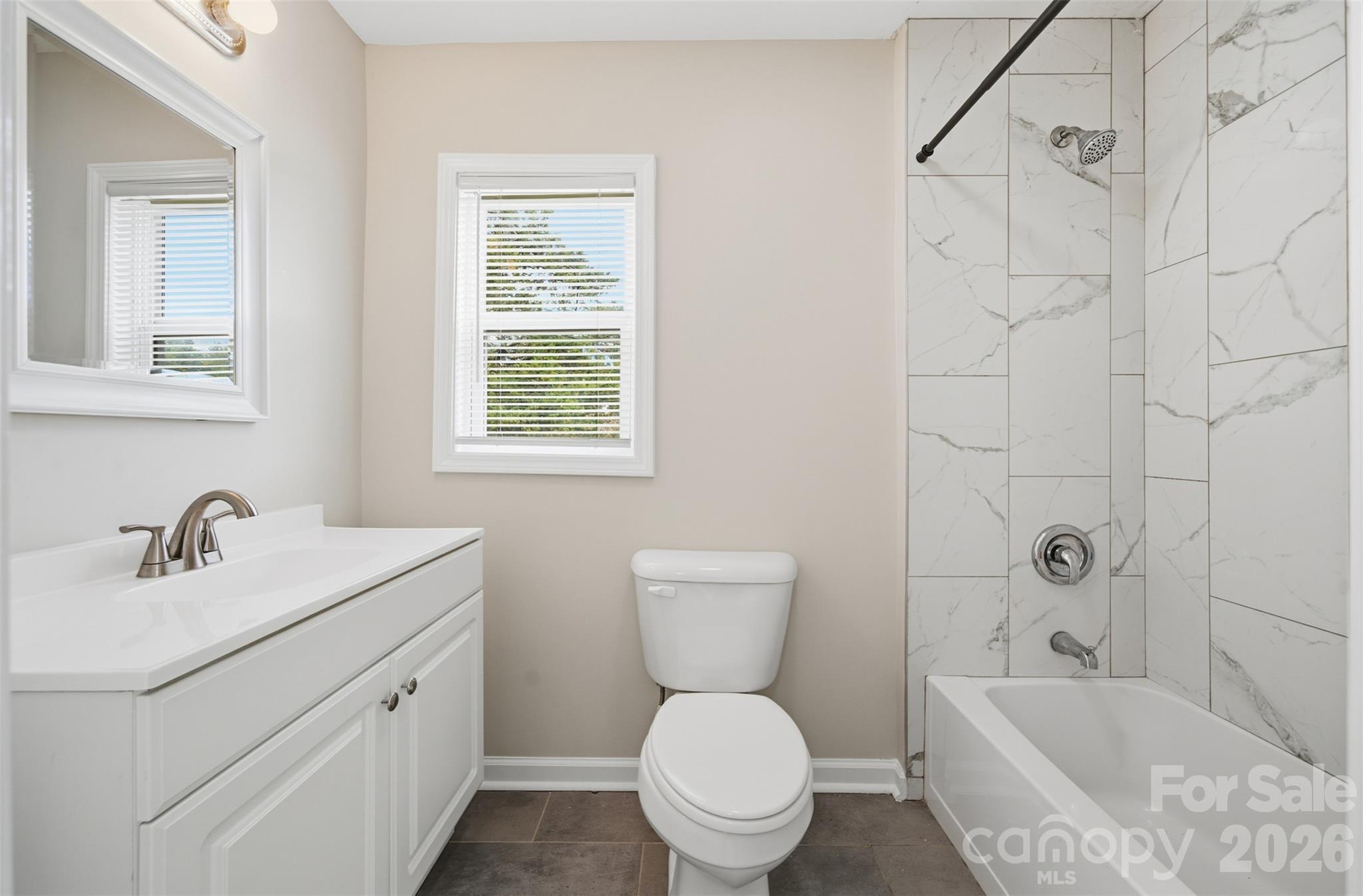 Bathroom with white vanity, toilet, and bathtub lined with marble-look tile.