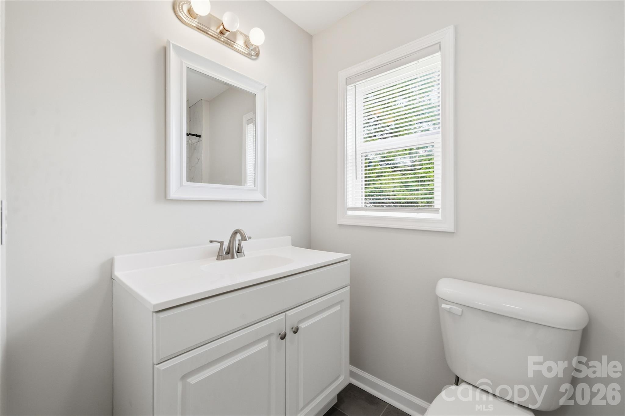 Bathroom with a white vanity and toilet beside a window with blinds.